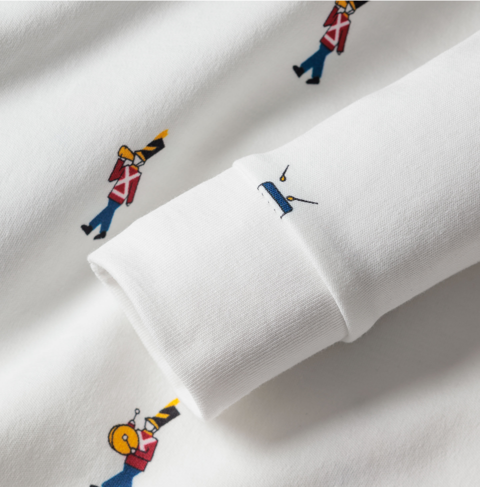 A close-up of a white garment featuring a pattern of small, colorful marching band figures and a blue drum embroidered near the cuff.