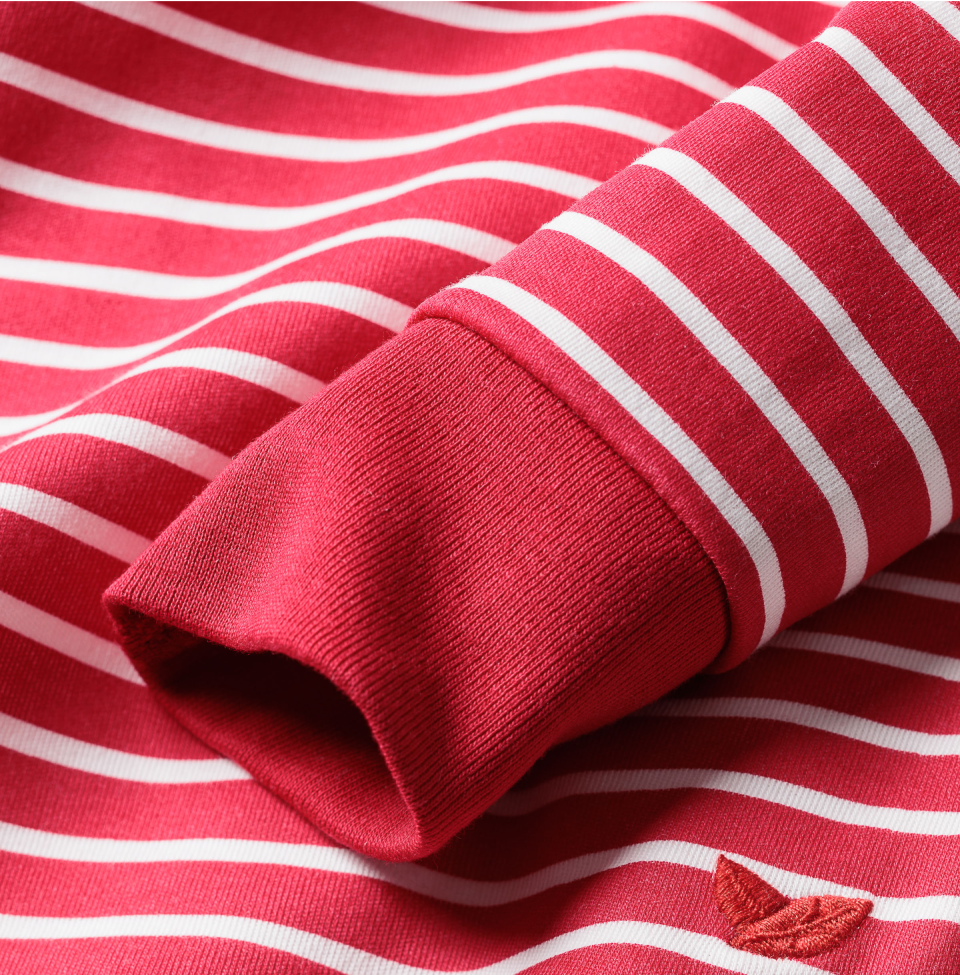 A close-up of a red and white striped fabric, showing the sleeve cuff of a shirt or sweater. The material appears soft, with a small decorative leaf detail embroidered near the cuff.