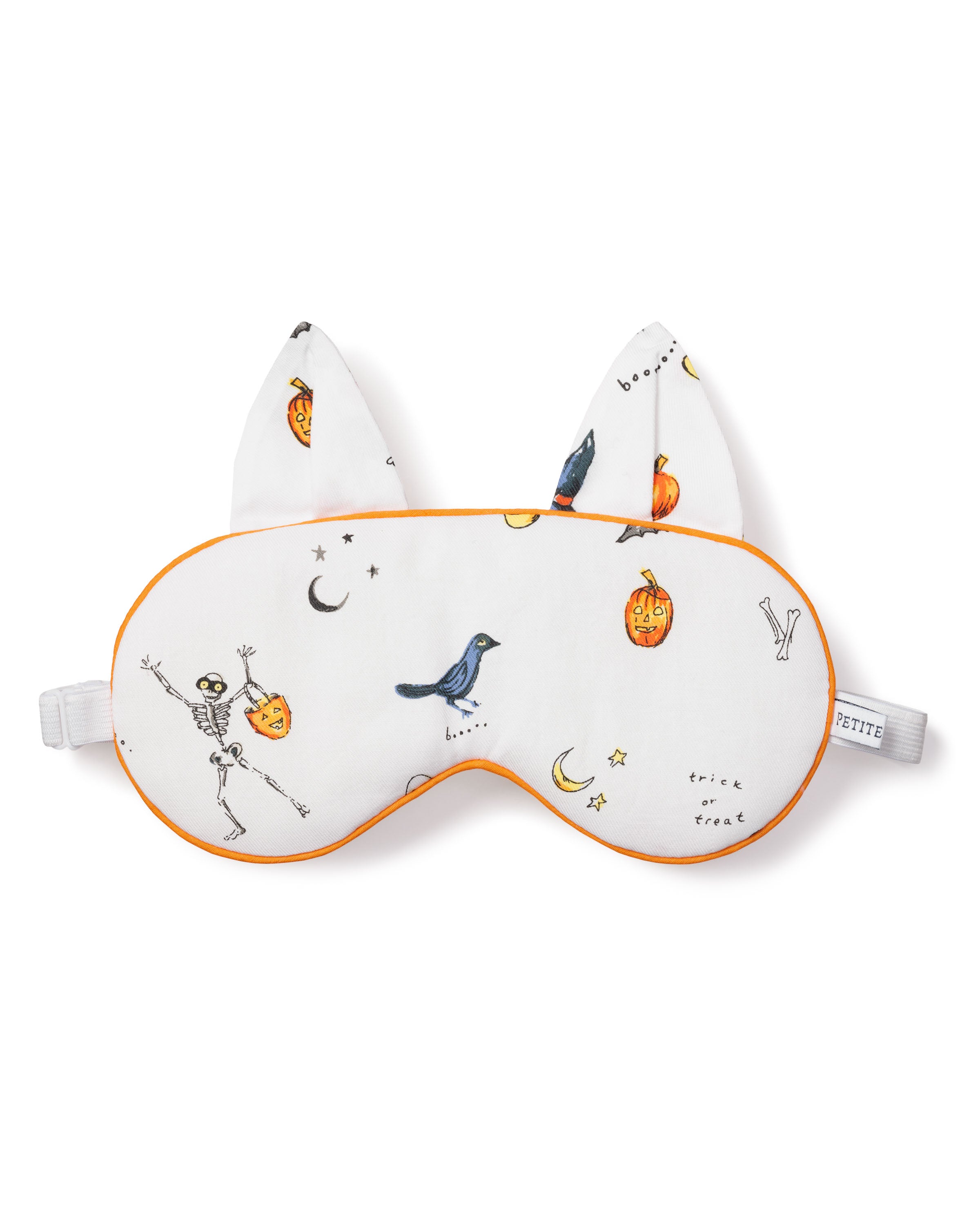 The Petite Plume Adults Twill Kitty Sleep Mask in Trick or Treat features a white design with orange trim, festive icons like a skeleton, bird, bats, pumpkins, stars, and trick or treat text. With cat ears and an adjustable strap, it adds spooky style to your sleep routine!.