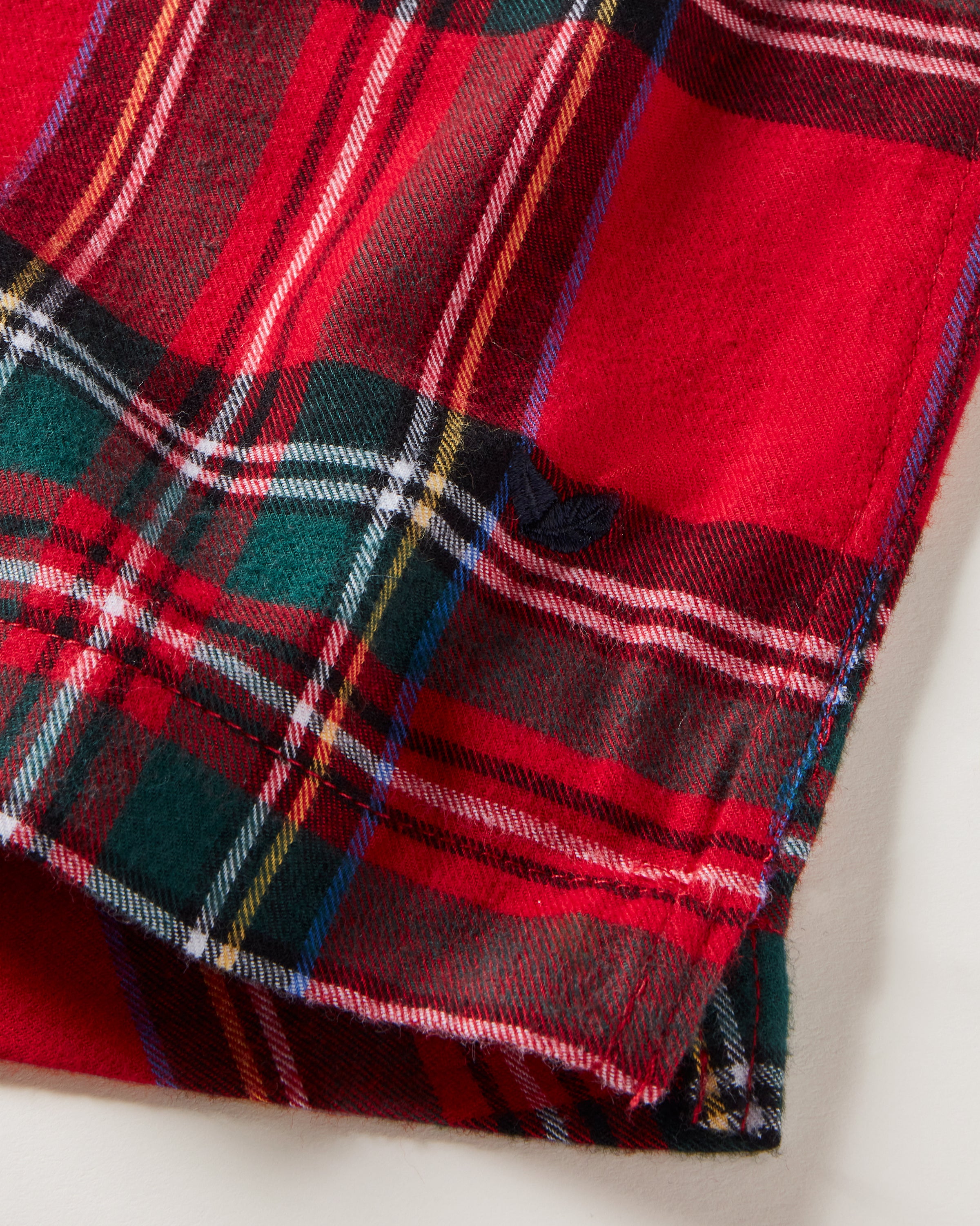 Close-up of Petite Plumes Mens Twill 3 Pack Boxers in Holiday Red, showcasing a red tartan fabric with a classic plaid pattern in green, white, blue, and yellow stripes. The folded corner reveals the textured woven cotton twill, perfect for a cozy boxer set!.