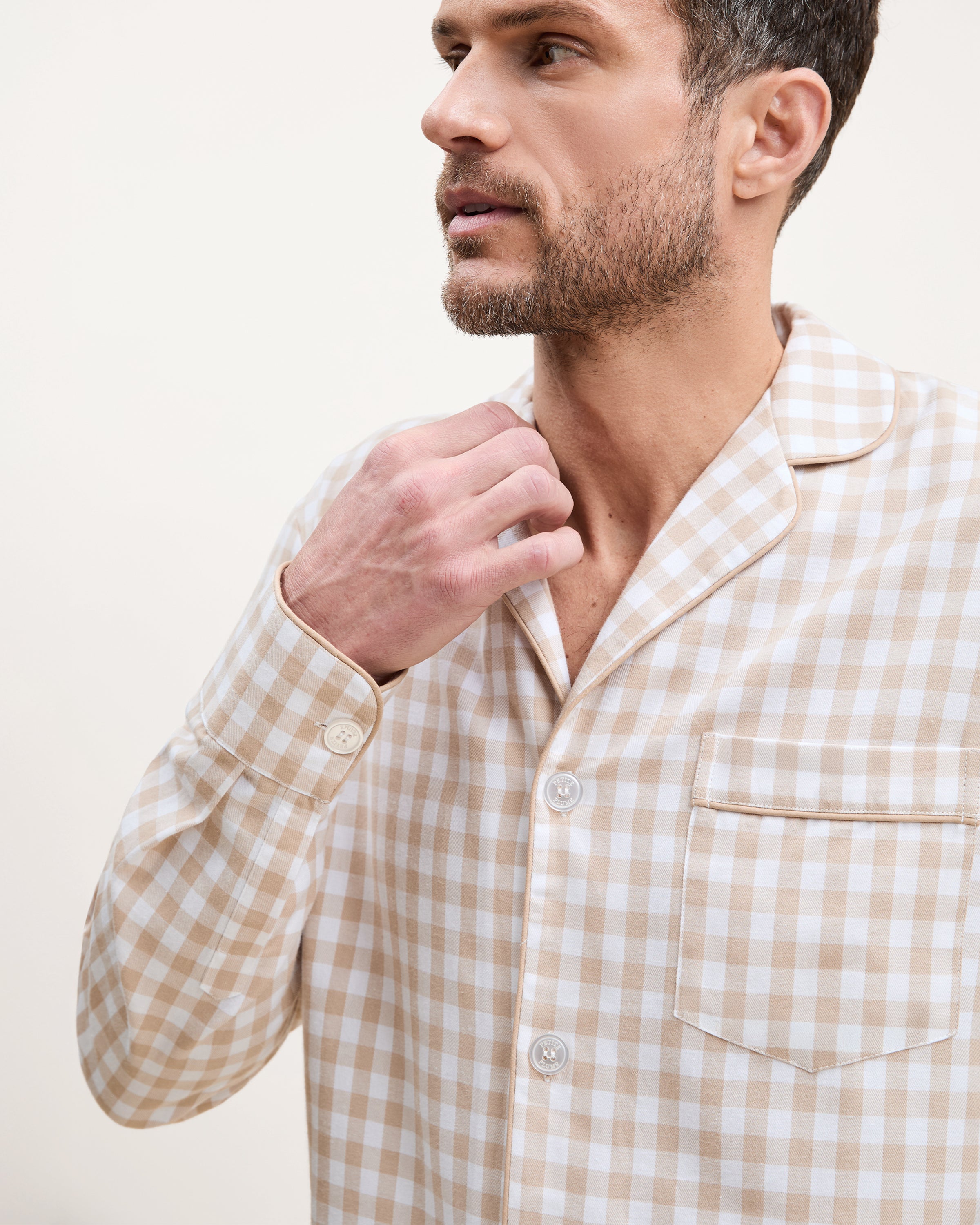 The Men's Twill Pajama Set in Camel Gingham includes a long-sleeve, button-up top with a chest pocket and matching pants, both in a beige and white gingham check pattern.