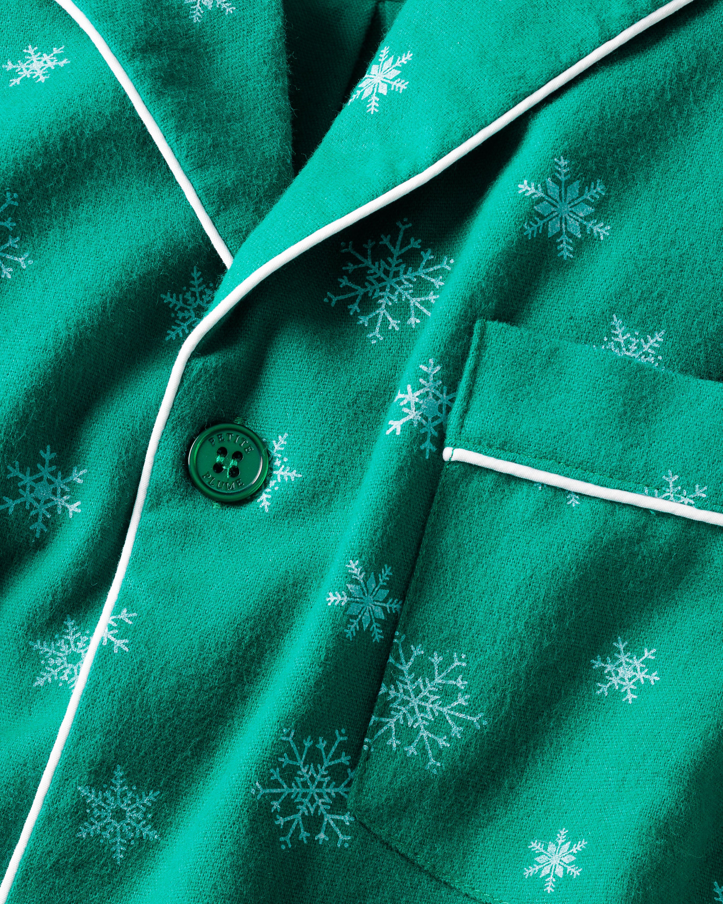 The Mens Flannel Pajama Set in Emerald Wonderland by Petite Plume features an emerald green fabric adorned with white snowflakes, a button, and a pocket. It has white piping along the edges, highlighting the exquisite quality cotton.