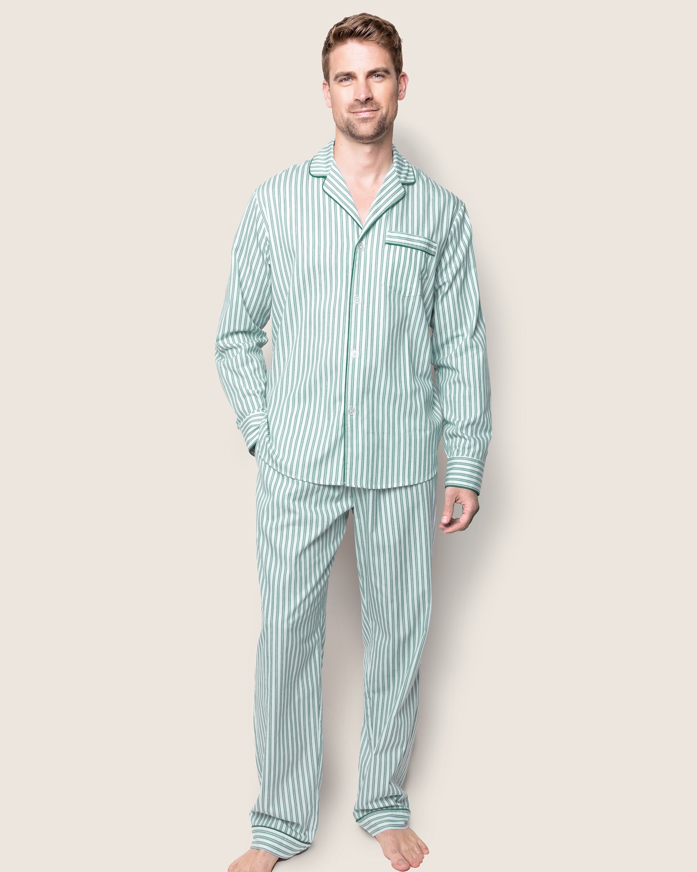 The Mens Twill Pajama Set in Emerald Ticking by Petite Plume features a close-up view of striped cotton fabric with vertical light blue and white lines, a French ticking pattern, green piping edges, three white buttons, and a right-side pocket.