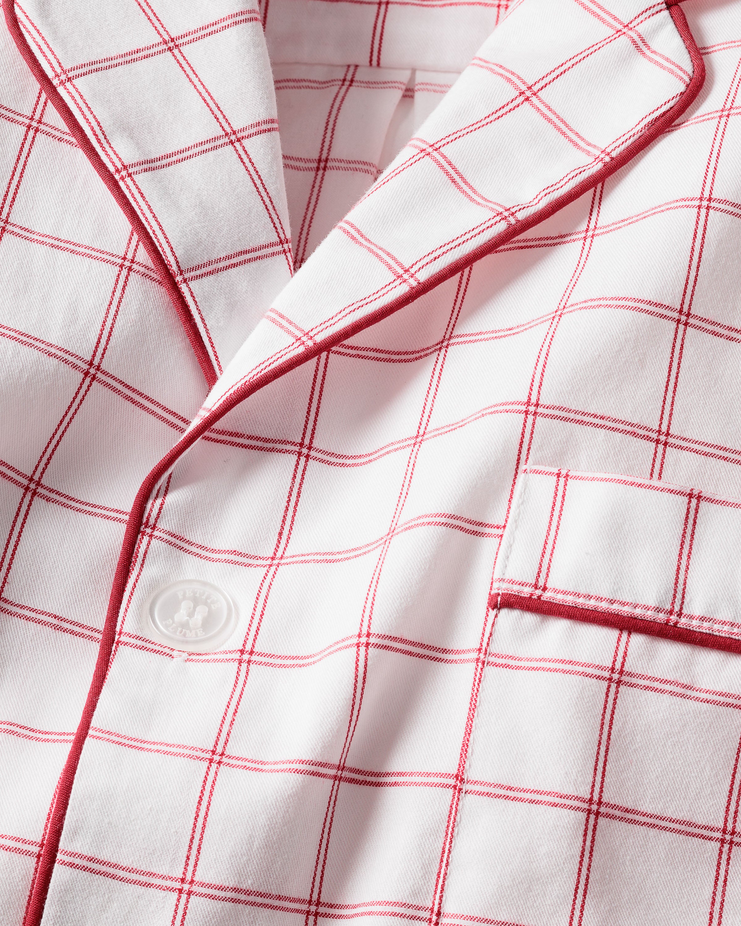 Close-up of Petite Plumes Mens Twill Pajama Set in Garnet Tattersall, made from 100% cotton twill. It features a collar, button, pocket, and neatly stitched grid-like garnet-red plaid design.