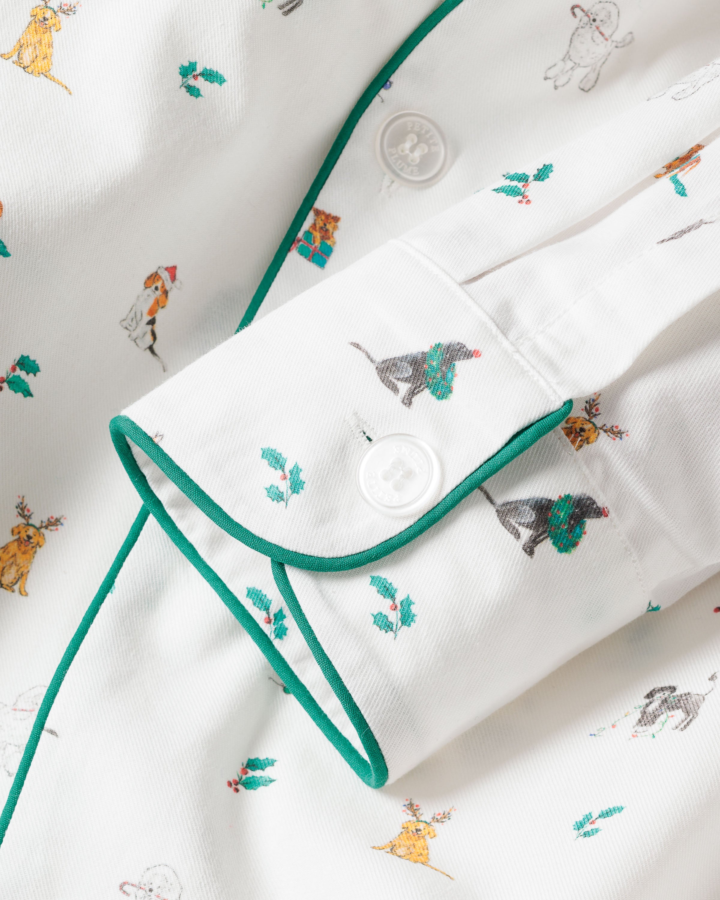 Close-up of a Mens Twill Pajama Set in Jingle Paws by Petite Plume, featuring colorful animal illustrations like a cat, dog, and deer with winter accessories on premium white cotton. The shirt has green piping and white buttons on the cuff, perfect for festive holiday wear.