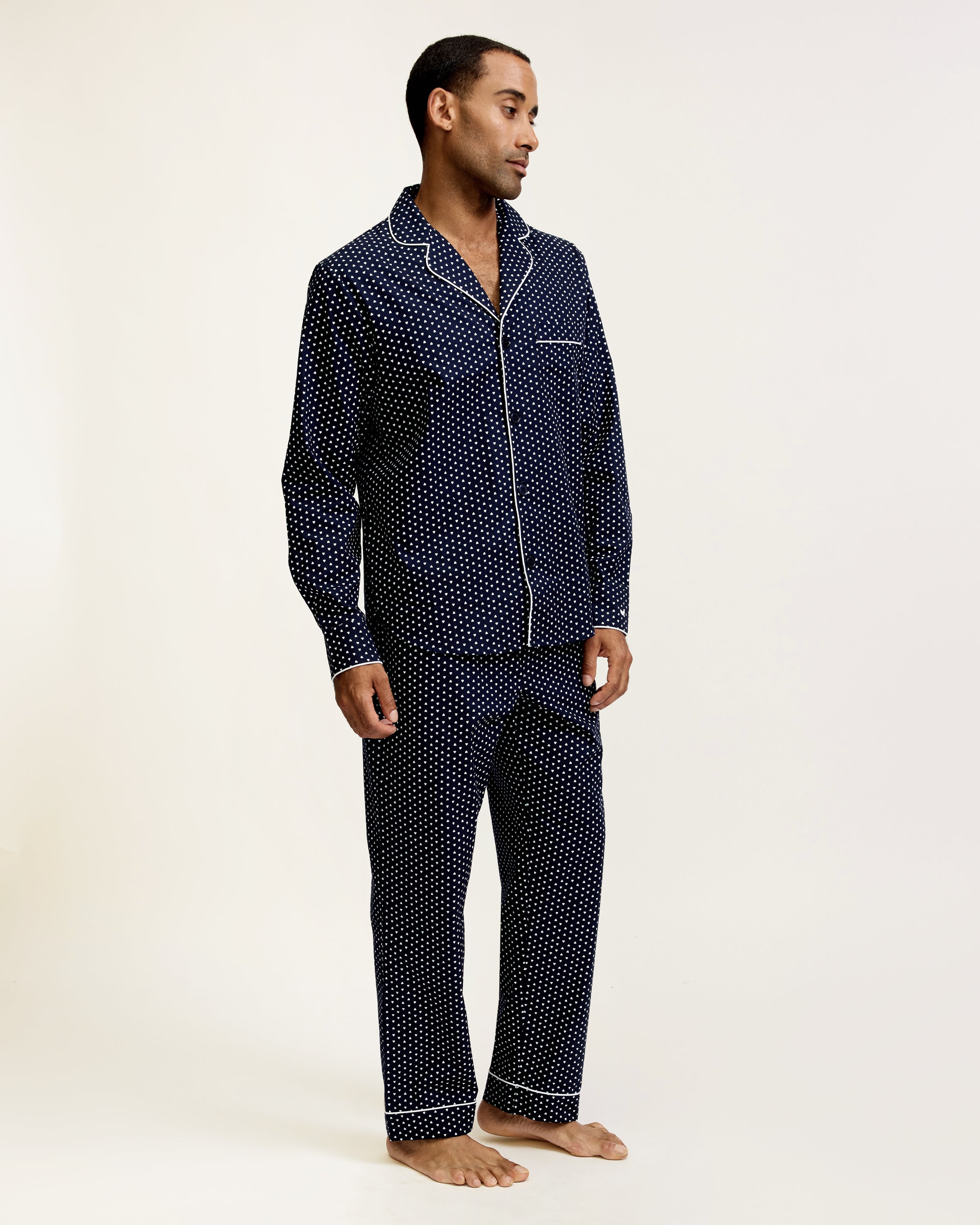 The Men's Twill Pajama Set in Midnight Hearts features a long-sleeve button-up top and pants, both navy blue with a small white polka dot pattern and white piping details.