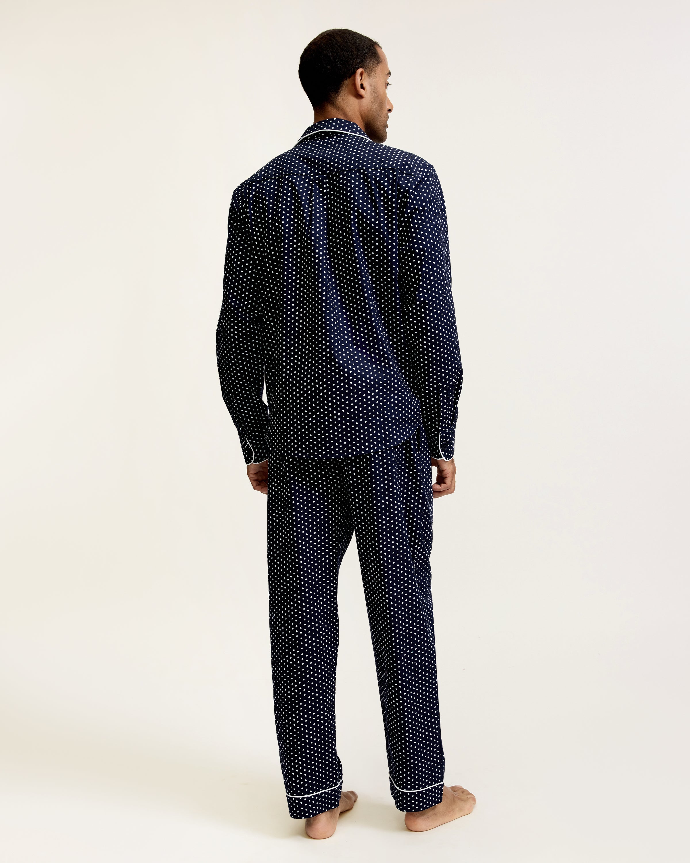 The Men's Twill Pajama Set in Midnight Hearts features a long-sleeve button-up top and pants, both navy blue with a small white polka dot pattern and white piping details.