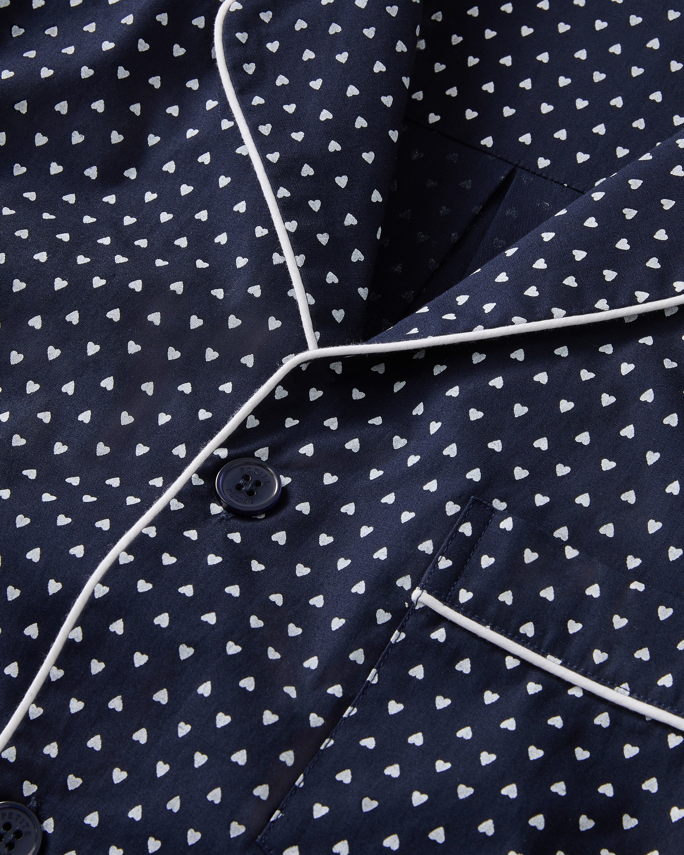 The Men's Twill Pajama Set in Midnight Hearts features a long-sleeve button-up top and pants, both navy blue with a small white polka dot pattern and white piping details.