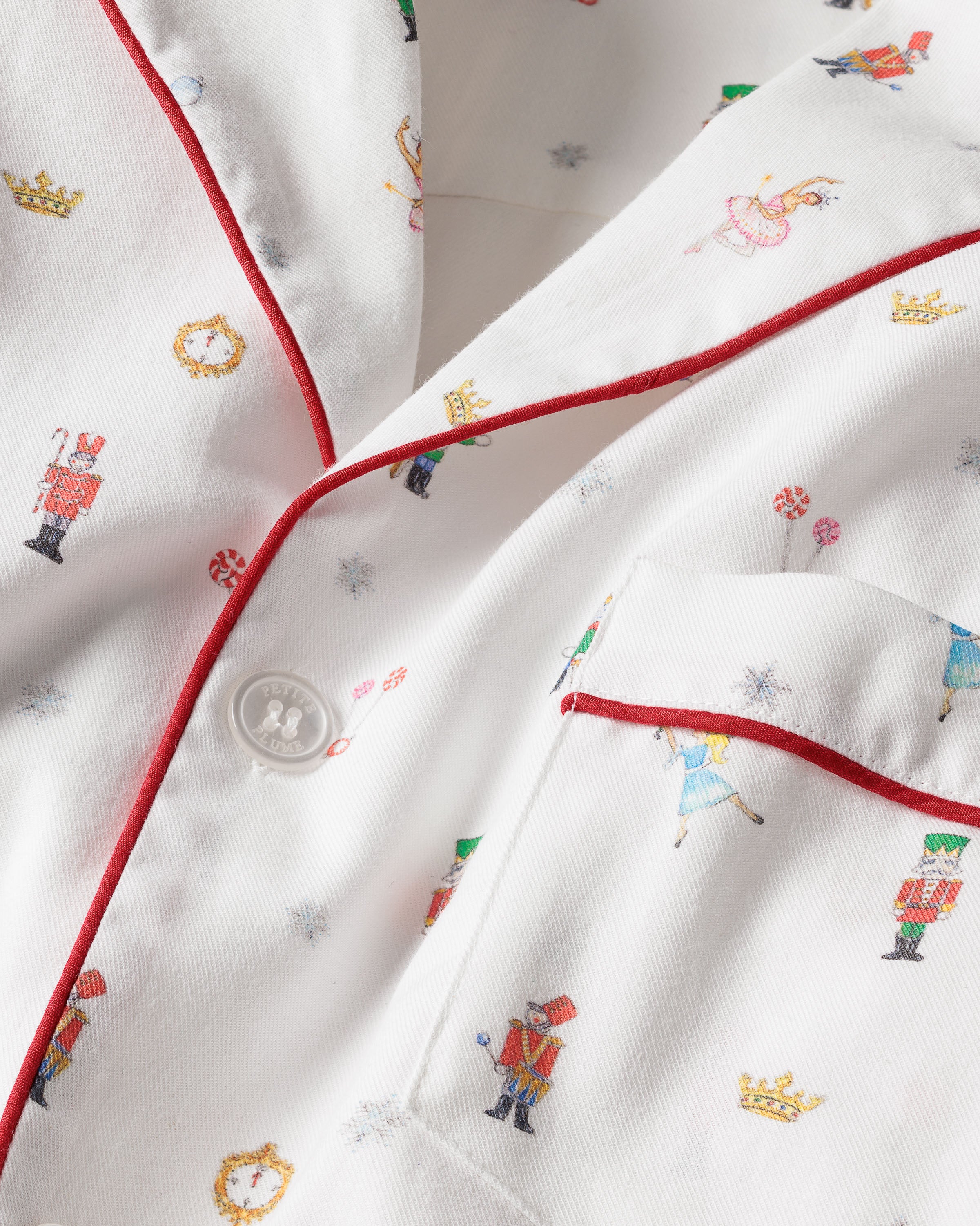 This close-up features the Mens Twill Pajama Set in A Night at the Nutcracker by Petite Plume, made of luxury cotton twill with festive toy soldier and ballerina prints. Red piping and a white pocket button add to its colorful, whimsical holiday charm.
