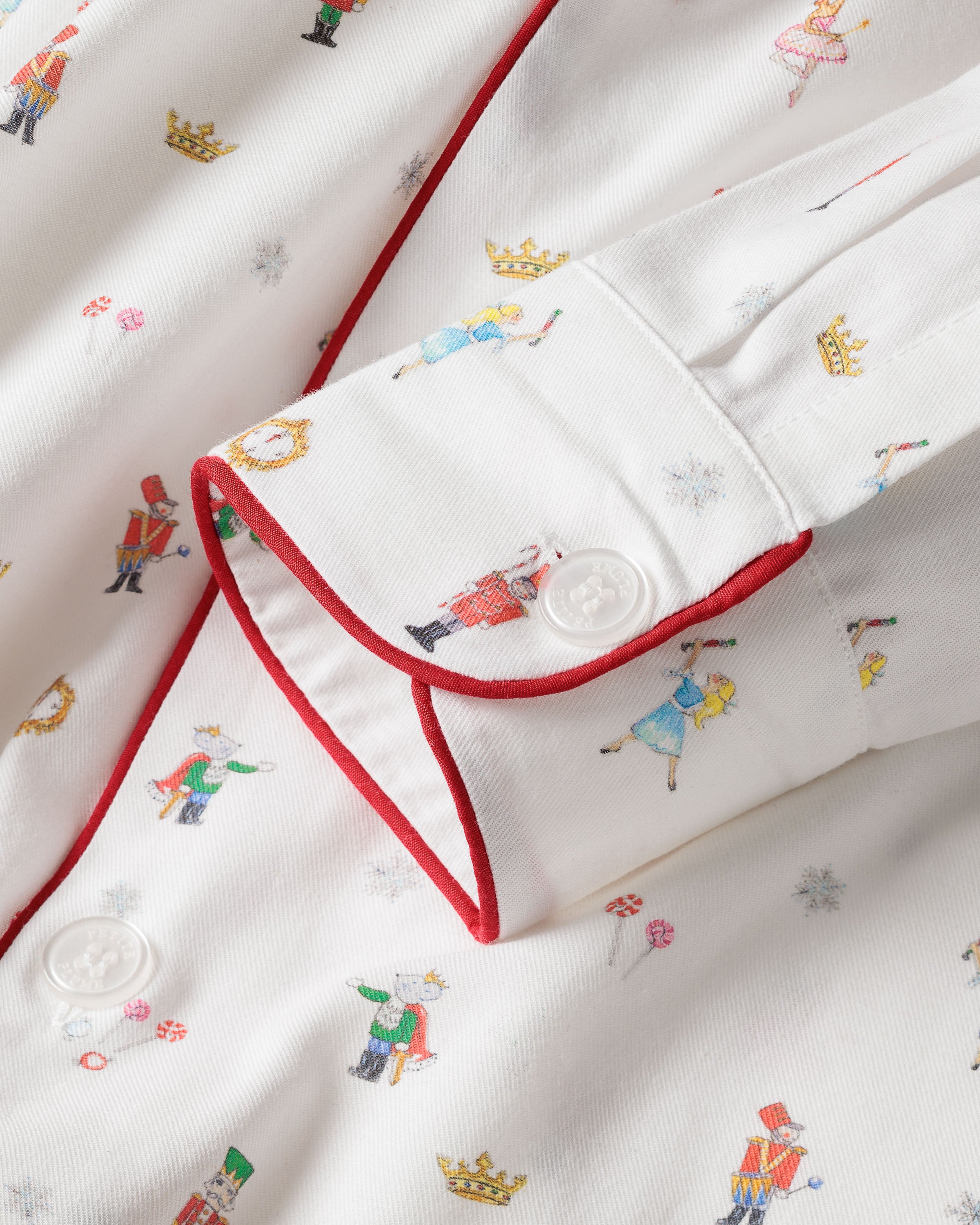 Close-up of the Mens Twill Pajama Set in A Night at the Nutcracker by Petite Plume, featuring luxury white cotton twill with colorful dancers and crowns, red piping, and a white cuff button for ultimate comfort and style.