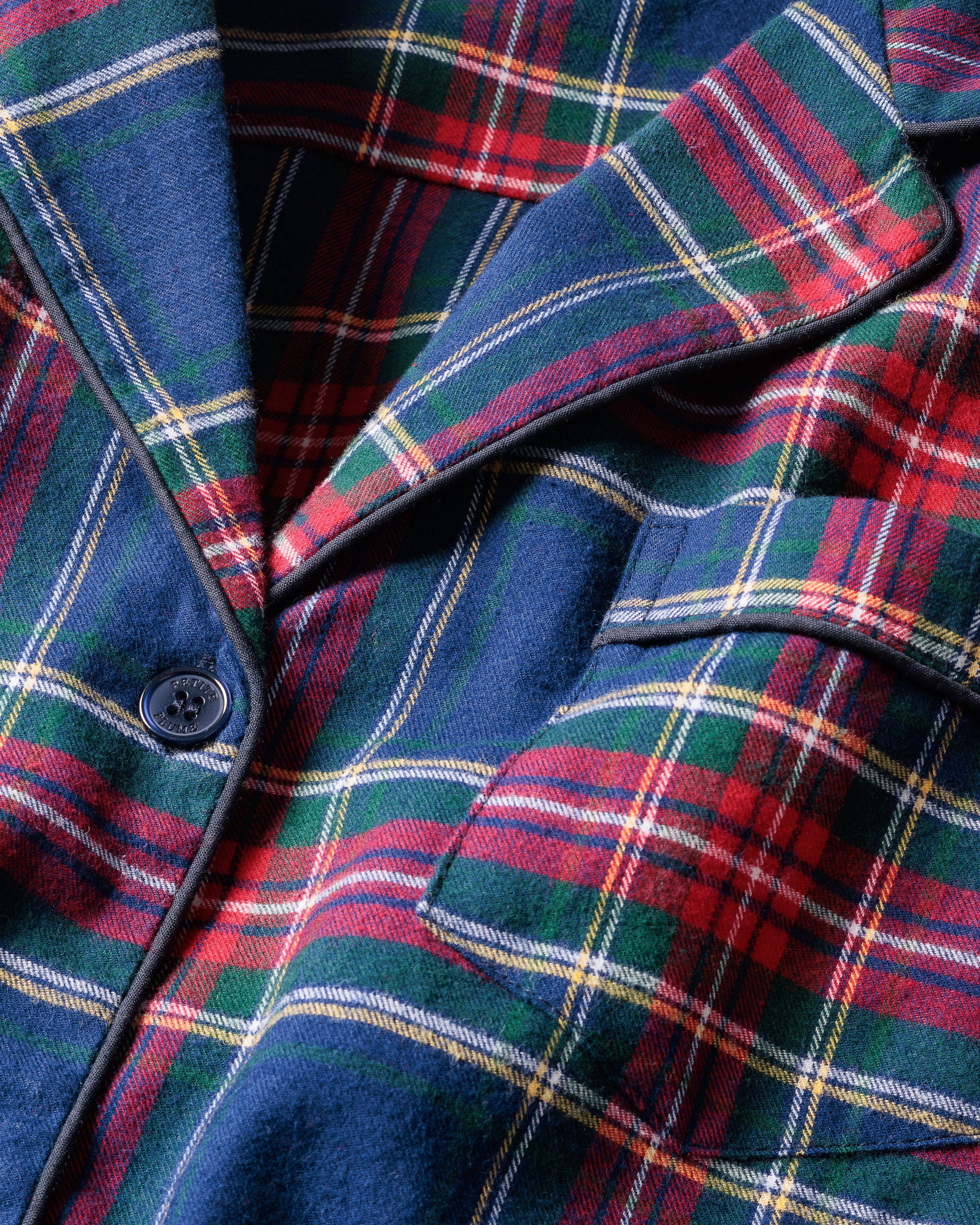 Close-up of a lightweight flannel plaid fabric with red, green, blue, and yellow stripes. The pattern is from Petite Plumes Mens Brushed Cotton Pajama Set in Windsor Tartan, featuring a notched lapel and a single black button.