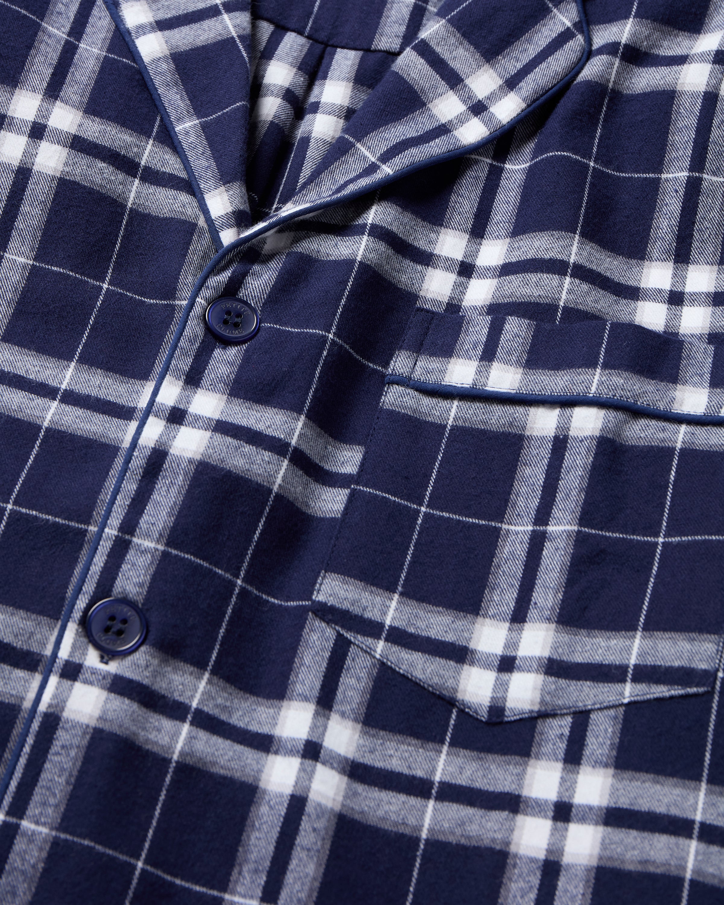 The Men's Brushed Twill Pajama Set in Oxford Tartan includes a two-piece navy and white plaid design with a long-sleeved button-up shirt featuring a chest pocket and matching drawstring pants.
