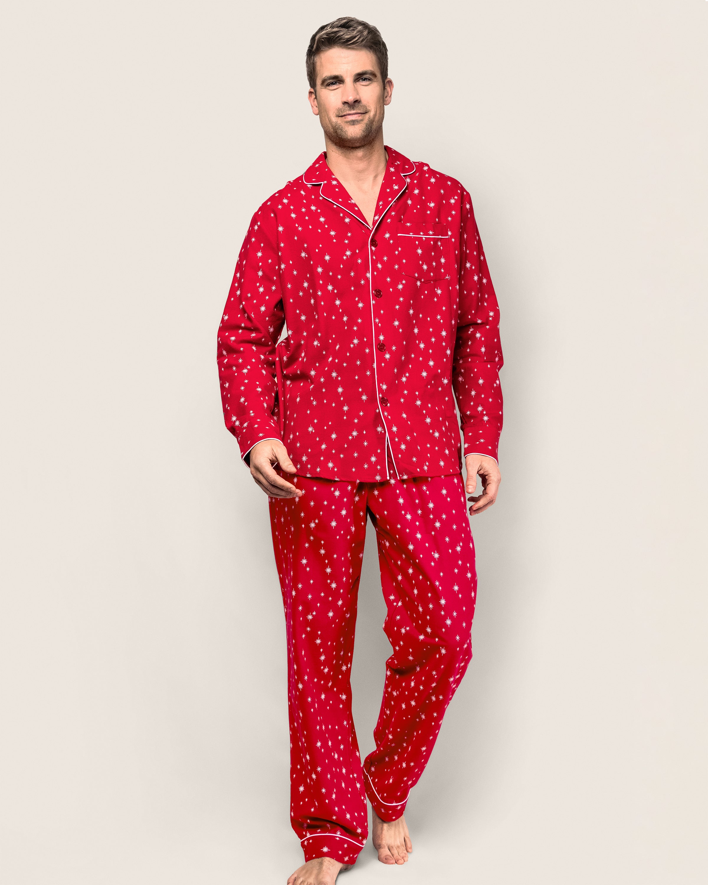 Barefoot against a plain light background, a man exudes calm in the Starry Night flannel pajama set by Petite Plume. His cozy attire complements his short hair and relaxed posture, adding an elegant touch to his look.