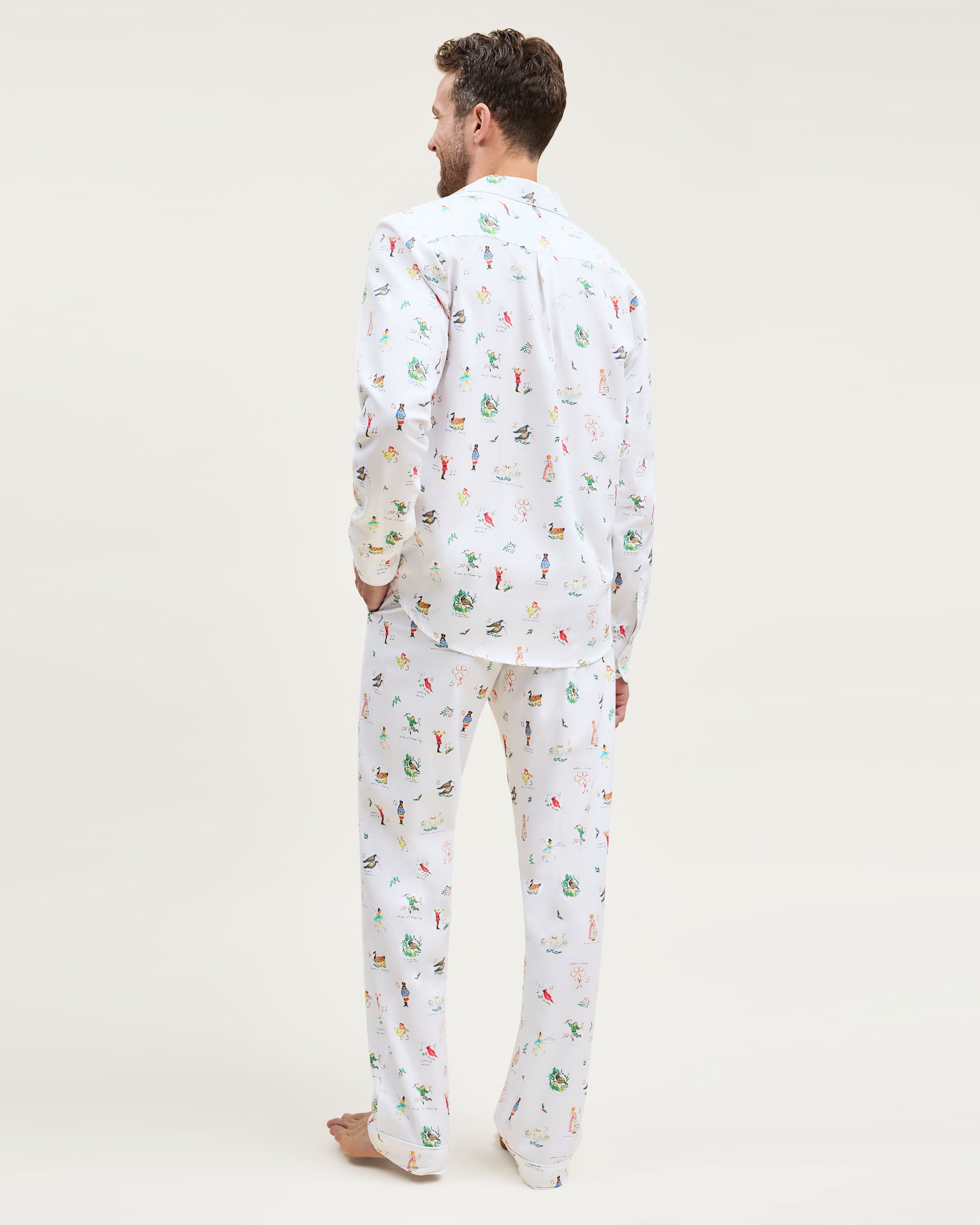 Men's Twill Pajama Set in 12 Days of Christmas: white button-up top and matching pants with a festive print featuring playful animals, palm trees, and people in various poses scattered across the fabric.