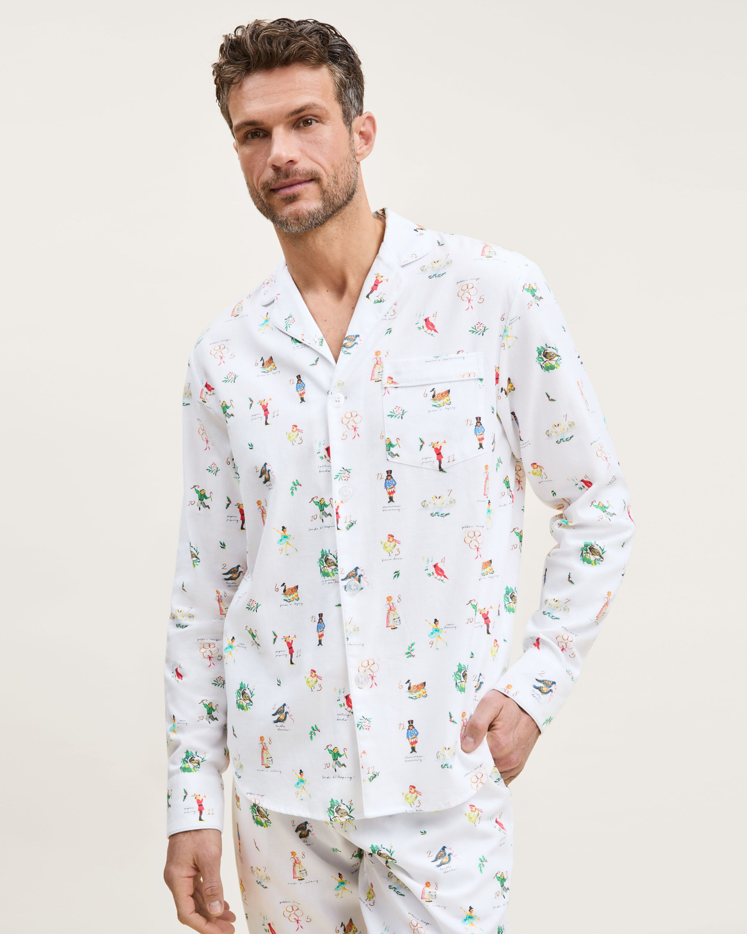 Men's Twill Pajama Set in 12 Days of Christmas: white button-up top and matching pants with a festive print featuring playful animals, palm trees, and people in various poses scattered across the fabric.