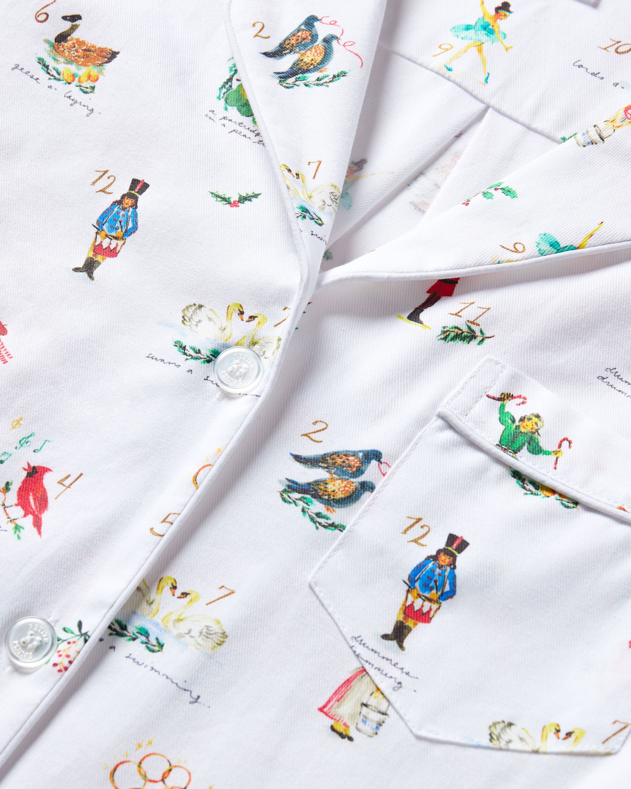 Men's Twill Pajama Set in 12 Days of Christmas: white button-up top and matching pants with a festive print featuring playful animals, palm trees, and people in various poses scattered across the fabric.