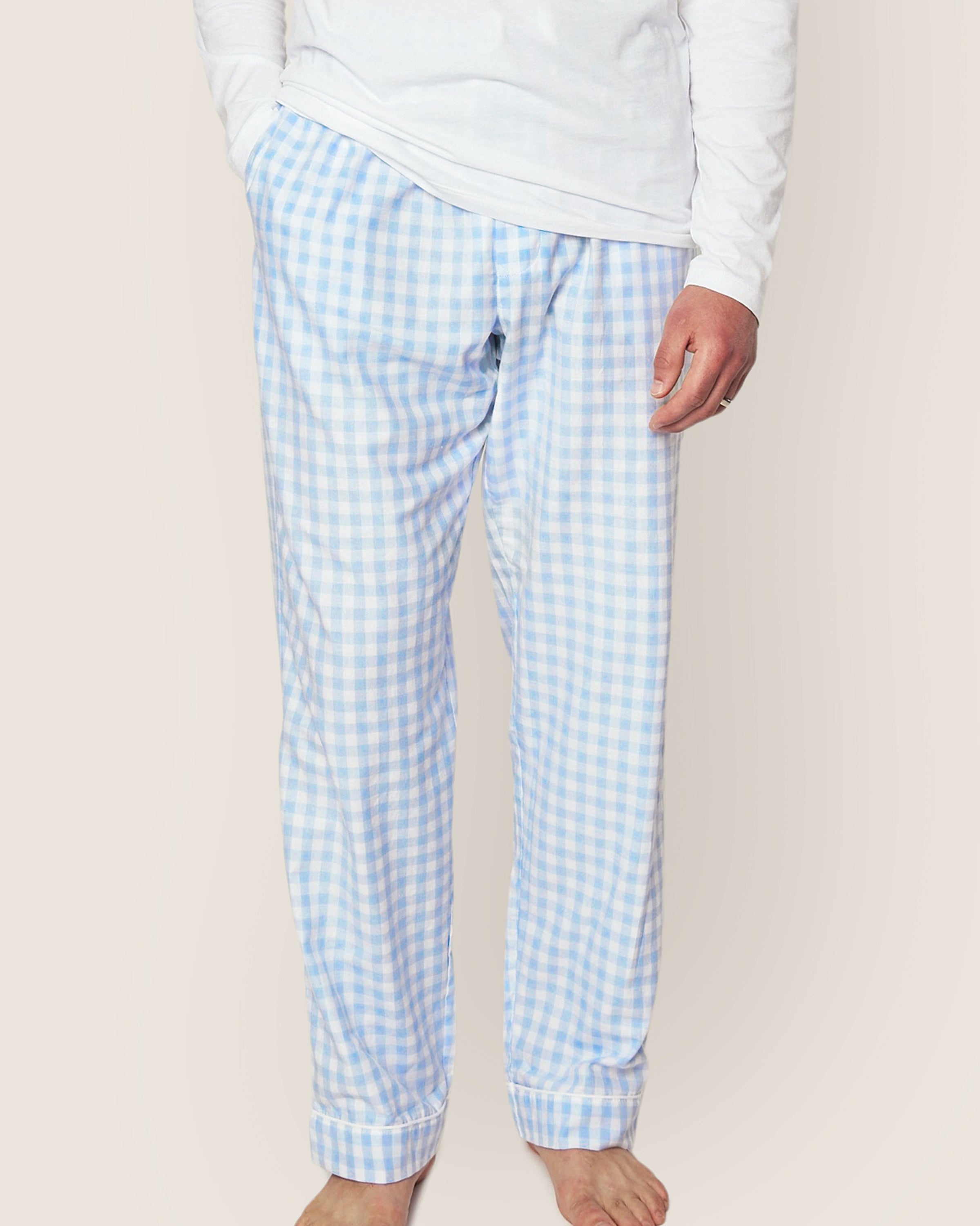 A person wears Petite Plumes luxurious twill pants in light blue gingham, featuring a relaxed fit and an elastic waistband, paired with a white long-sleeve shirt. They stand barefoot on a plain background, highlighting the finest quality cotton.