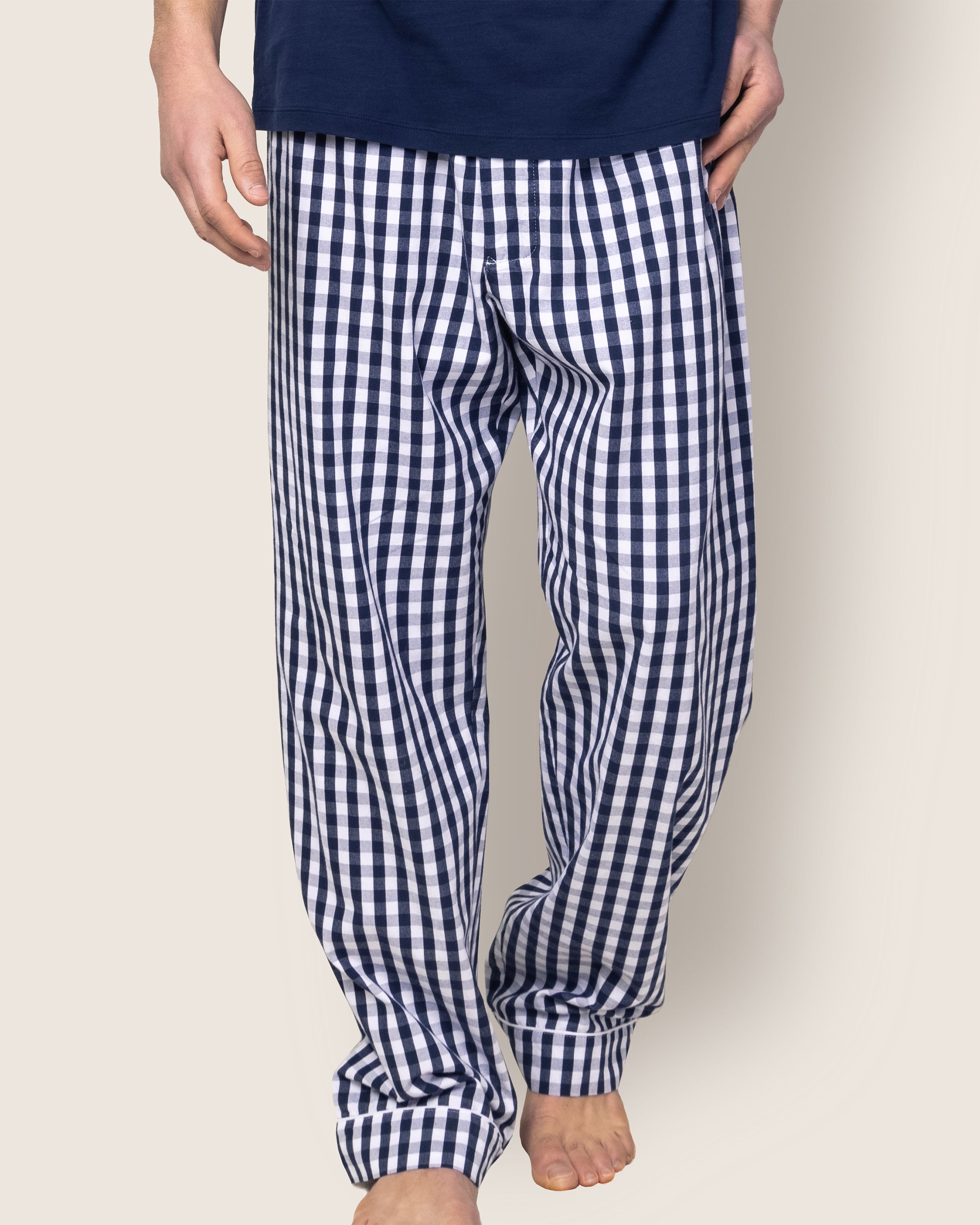 A person is wearing Petite Plumes Mens Twill Pajama Pant in Navy Gingham, barefoot, with a dark blue shirt visible on their upper body against a light beige background.