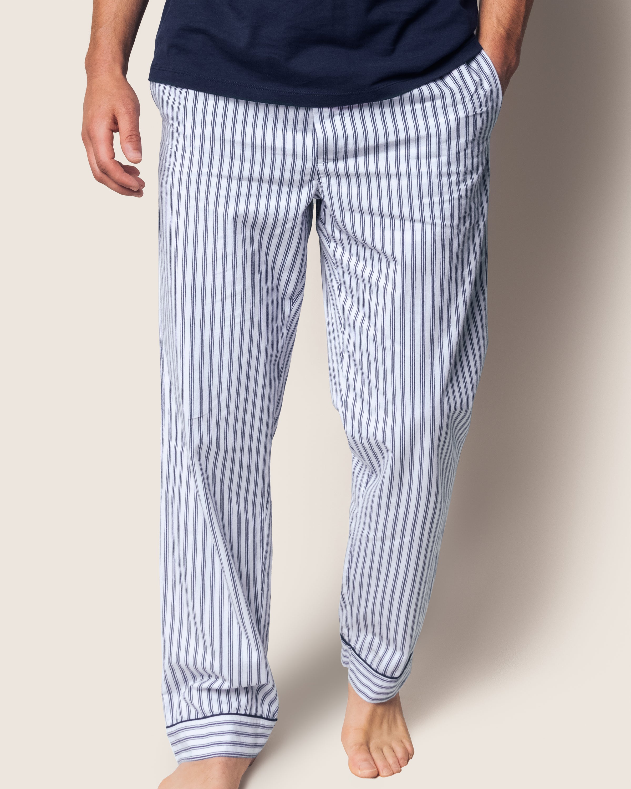 A person wearing Petite Plumes Mens Twill Pajama Pants in Navy French Ticking, hands in pockets, barefoot with a dark shirt against a plain, light background.