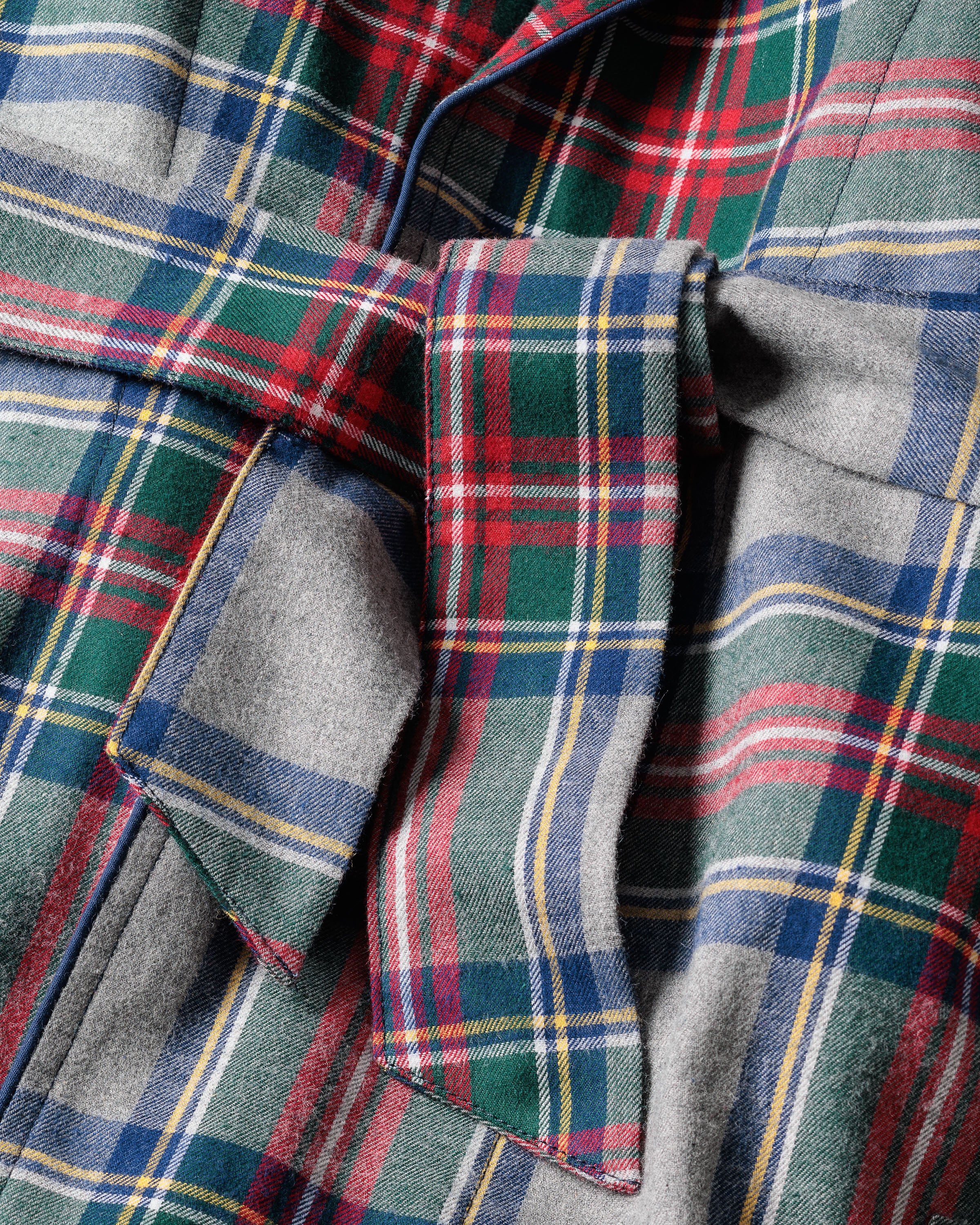 The Mens Brushed Cotton Robe in Westminster Tartan by Petite Plume features a close-up of its vibrant design with red, green, blue, and yellow lines. The soft cotton texture exudes elegance, reminiscent of luxury sleepwears attention to detail with a tied bow at the center.