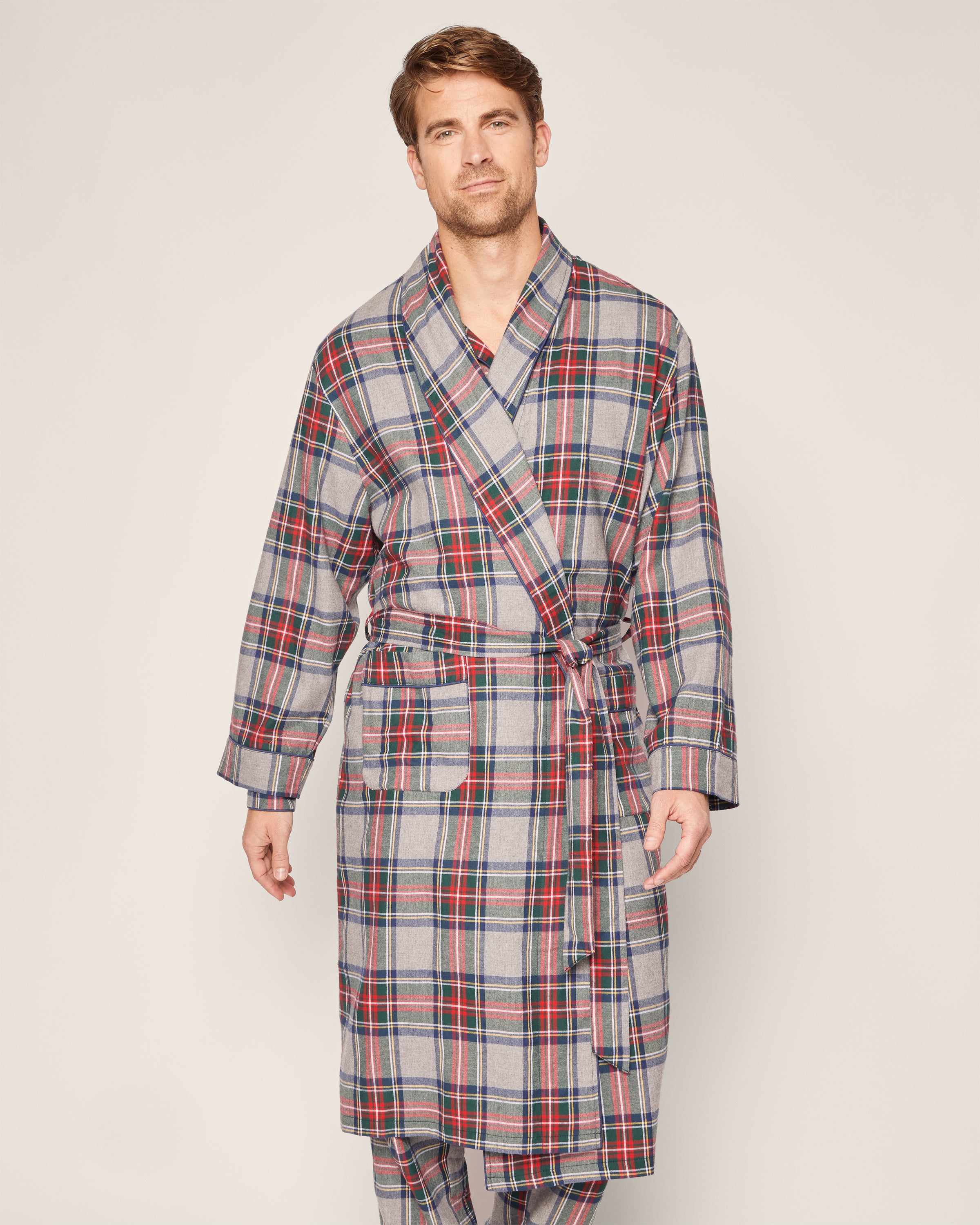 A person in a Petite Plume Mens Brushed Cotton Robe, showcasing the classic Westminster Tartan with red, blue, and gray lines, stands against a plain backdrop. The robe is tied at the waist, highlighting luxurious sleepwear as they appear relaxed and comfortable.