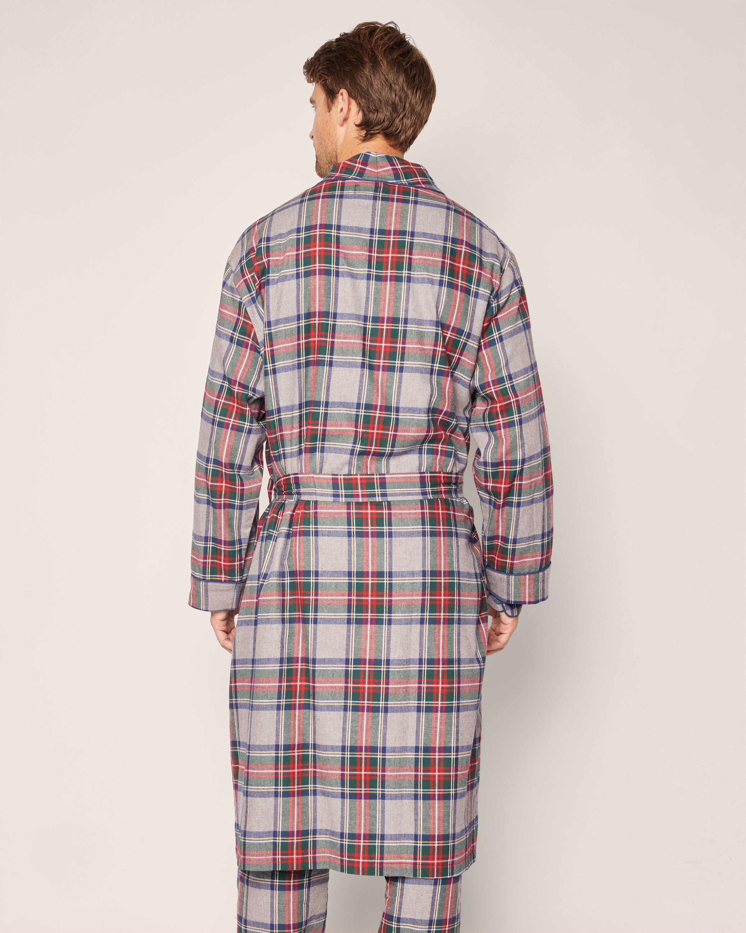 Clad in Petite Plumes Mens Brushed Cotton Robe in Westminster Tartan, a person, back to the camera against a neutral background, radiates elegance. The robe, featuring red, blue, and white plaid tones with a waist belt, captures the classic charm of luxury sleepwear.