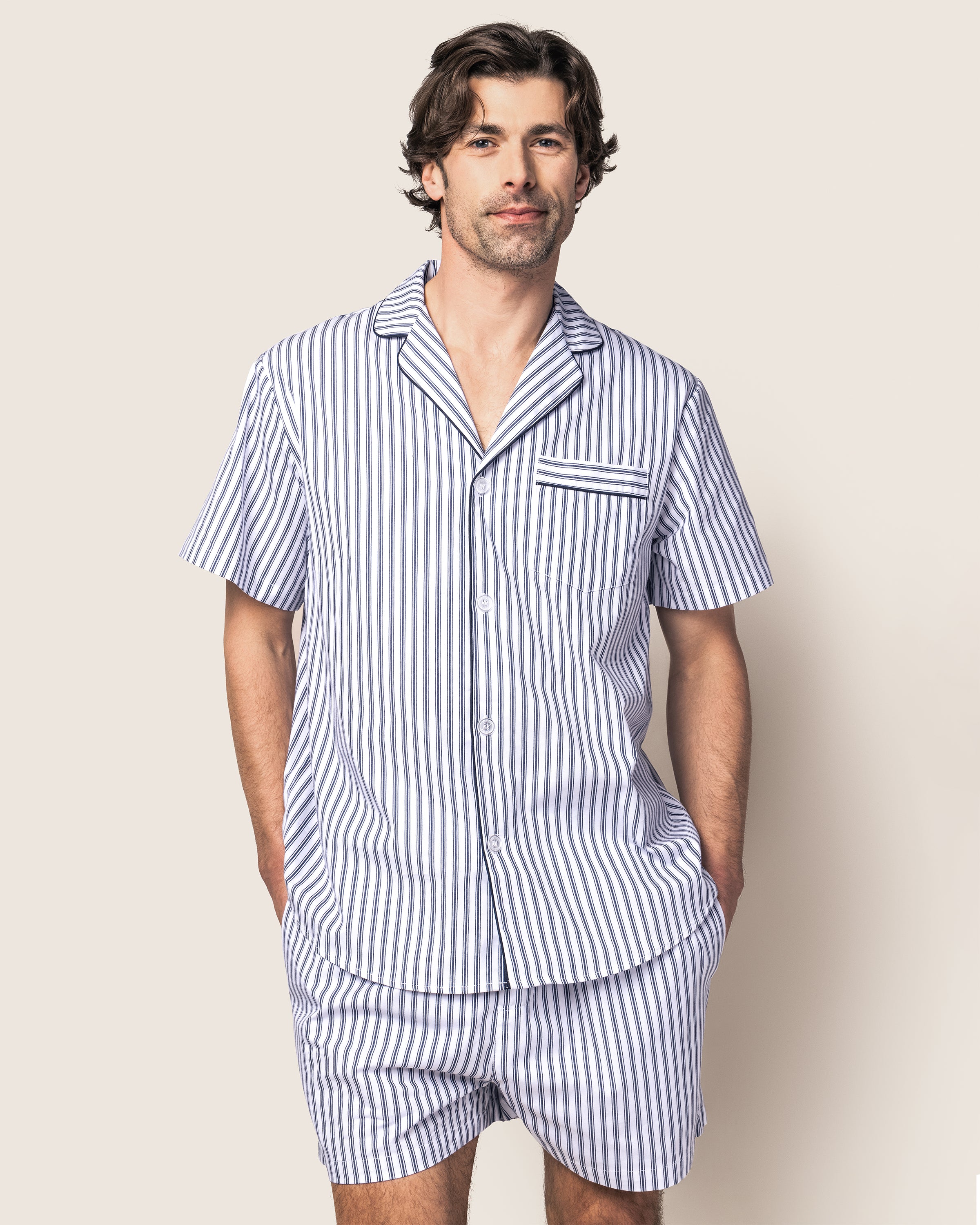 Indulge in the luxurious Mens Twill Pajama Short Set in Navy French Ticking by Petite Plume, featuring a short-sleeved button-up shirt with a pocket and matching shorts. Made from premium cotton, it showcases elegant blue and white stripes with a chic black drawstring on the shorts.