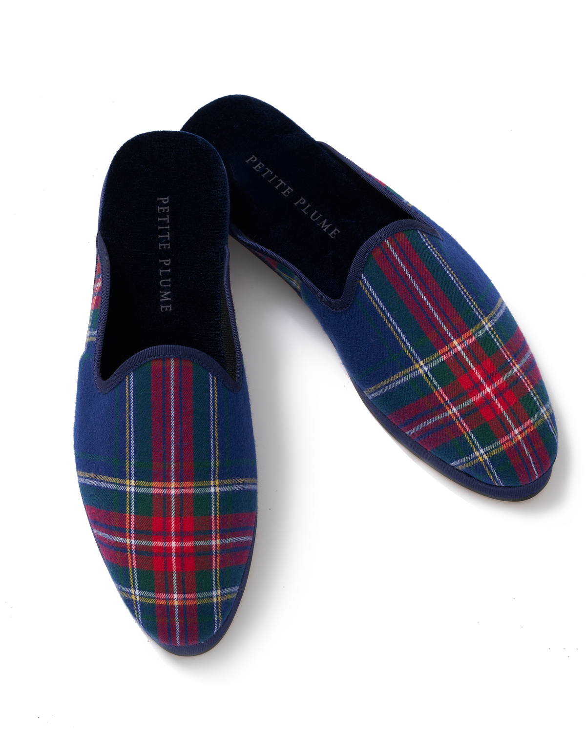 Women’s Slippers in Windsor Tartan are slip-ons with navy, red, green, and white plaid fabric and black insoles featuring PETITE PLUME in white letters.