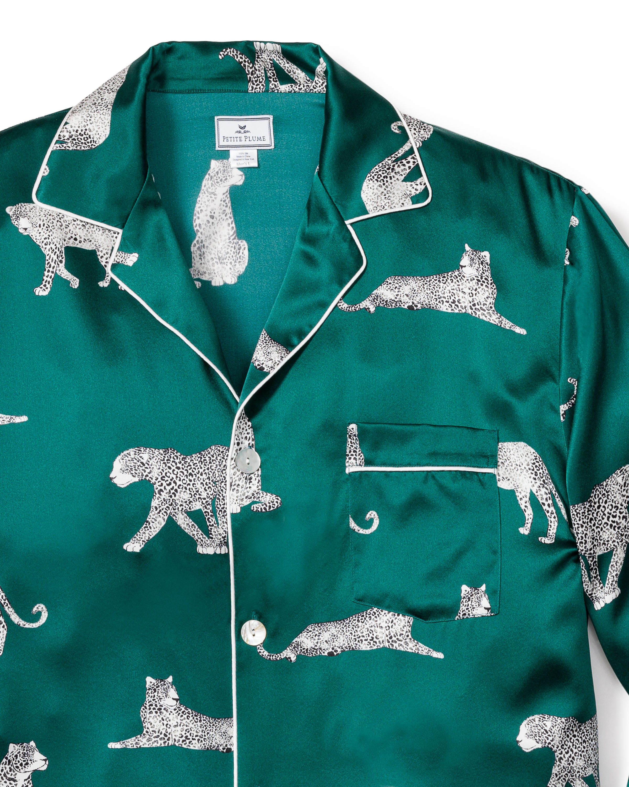 The Mens Silk Pajama Set in Panthère de Luxe by Petite Plume features a whimsical emerald green silk pajama shirt adorned with white leopards, elegantly detailed with white piping on the collar, pocket, and button line.