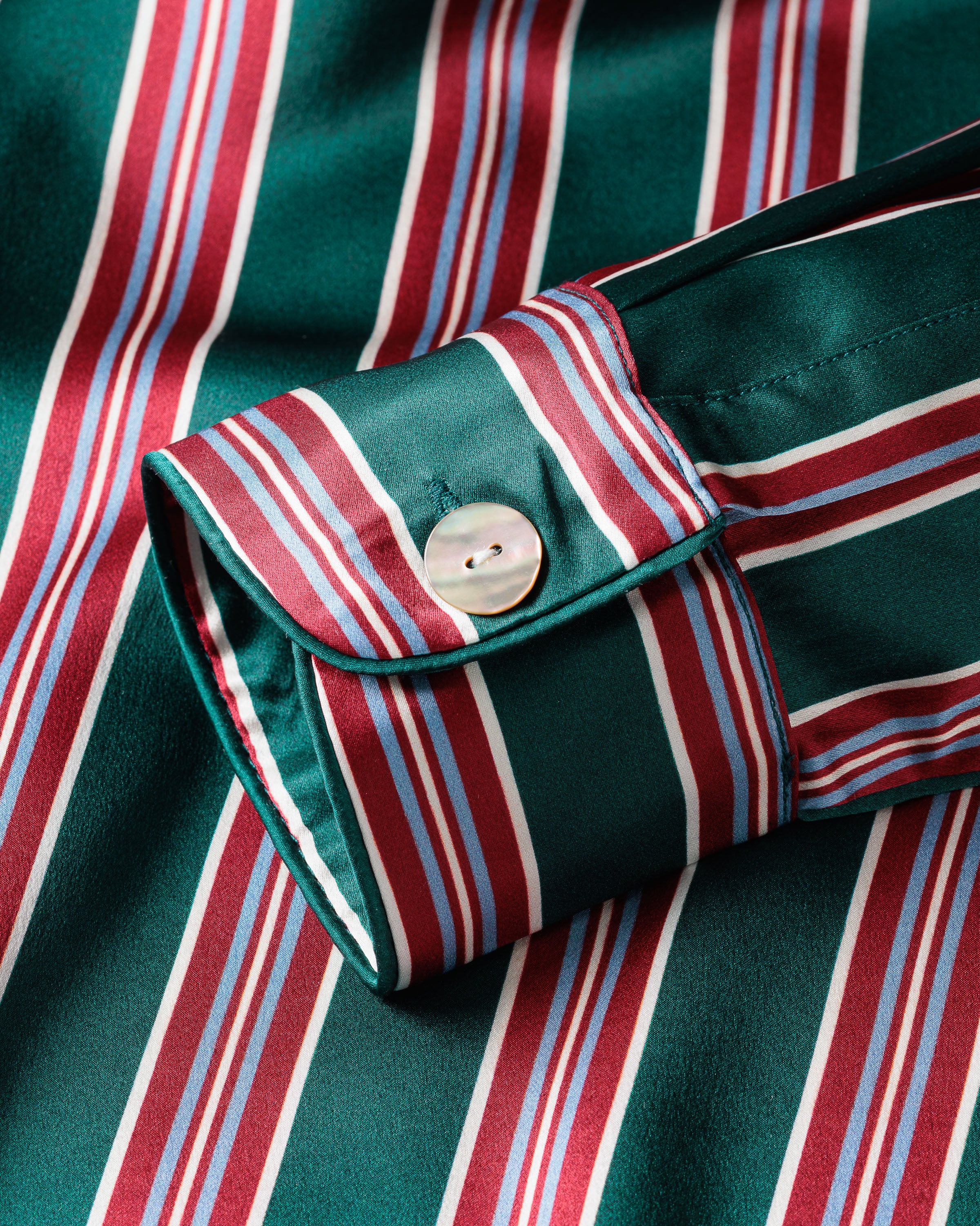 Close-up of a green long-sleeve shirt from the Petite Plume Mens Silk Pajama Set in Lancaster Stripe, featuring red, white, and blue vertical stripes. The cuff has a white button and the temperature-regulating silk gives it a smooth texture and slight sheen akin to luxurious sleepwear.