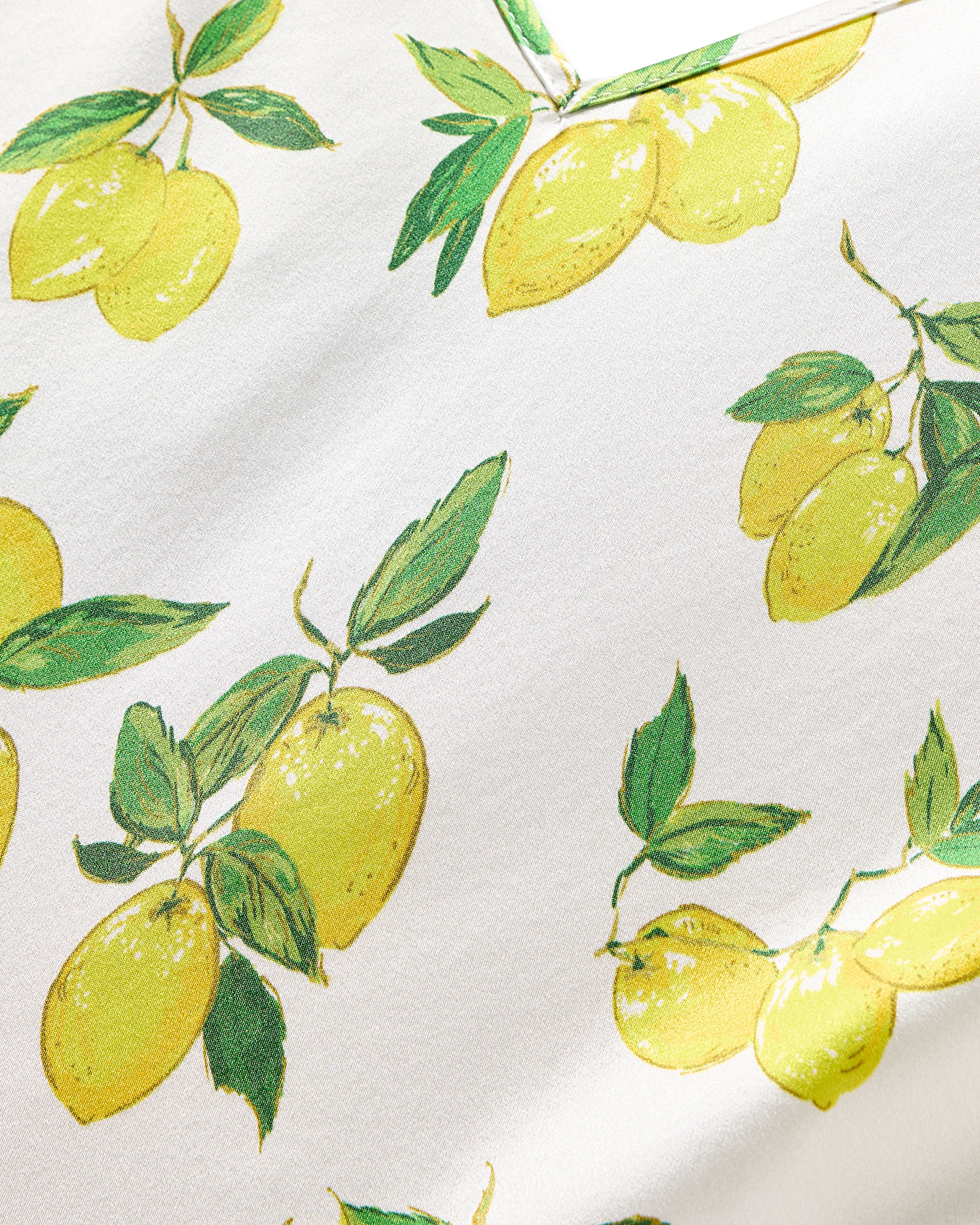 The Womens Silk Short Set in Amalfi Lemons by Petite Plume features a luxurious fabric adorned with vibrant yellow lemons and green leaves on a white background. The evenly spaced design adds elegance and style to this perfect silk sleepwear piece.