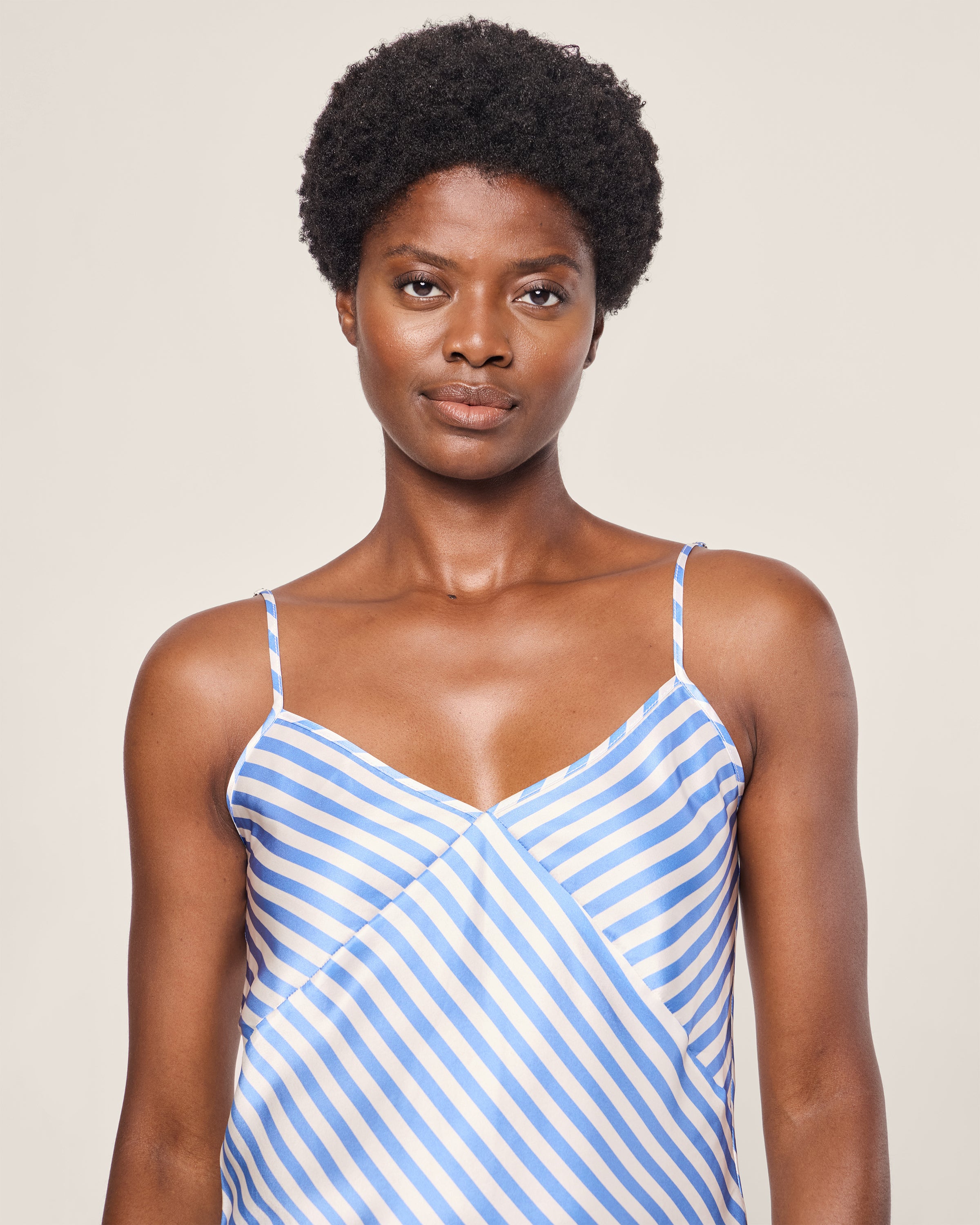 A person with short, curly hair wears the Womens Silk Cami Short Set in Azure Stripe by Petite Plume, standing against a plain background and looking toward the camera.