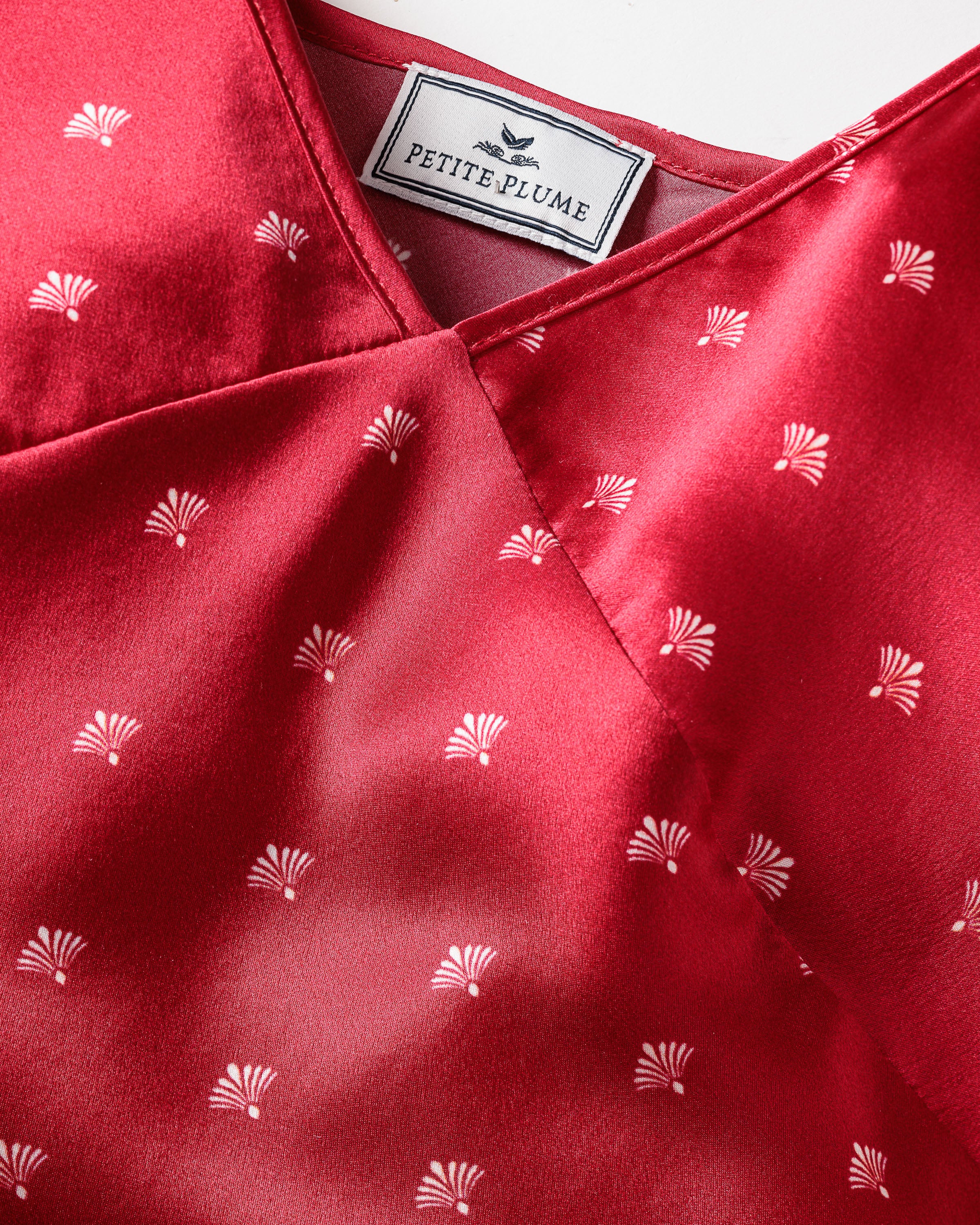 A close-up of a luxurious crimson garment from Petite Plume, this Womens Silk Cami Short Set in Art Nouveau style boasts a subtle white fan-shaped print and wrap-style neckline, ideal for those who seek elegance in nightwear.