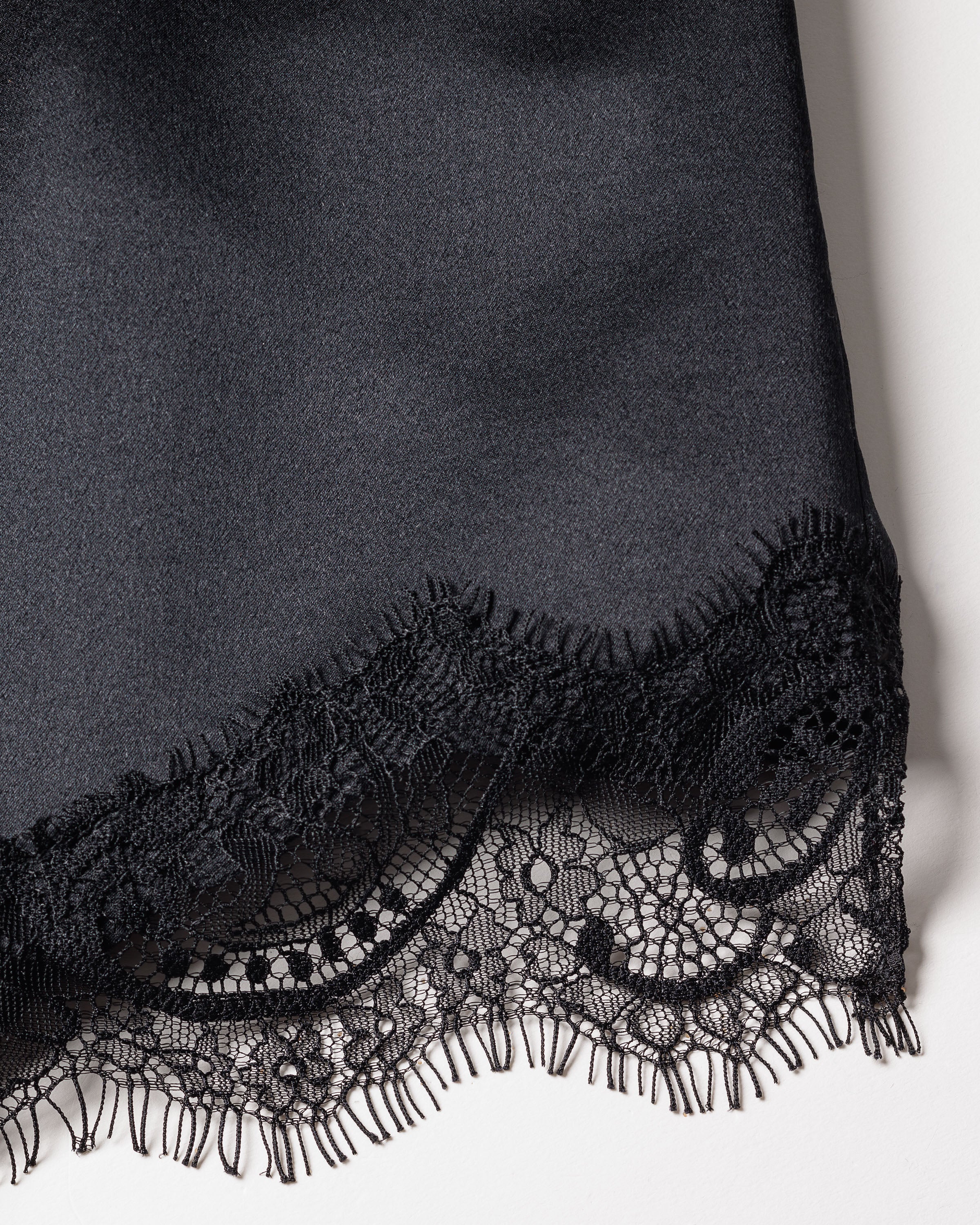 Close-up of the Womens Silk Lace Cami Short Set in Black by Petite Plume. This luxury silk sleepwear features intricate floral lace trim for elegance, a smooth satin-like finish, and is machine-washable for convenience. Contrasting textures of lace and solid fabric add visual interest.