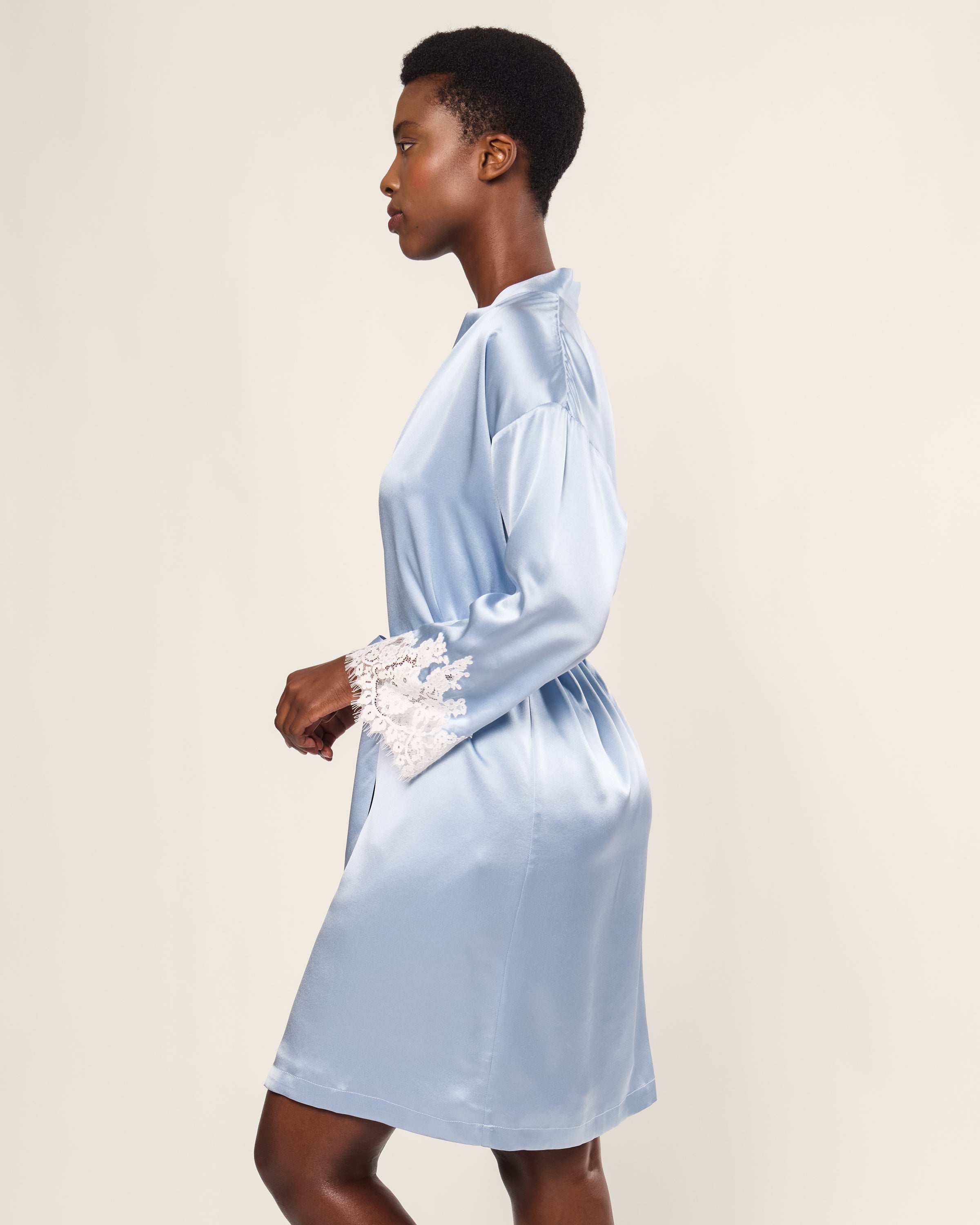 A woman in profile wears the Petite Plume Womens Silk Lace Robe in Periwinkle, featuring hypoallergenic properties and white lace cuffs, against a plain background.