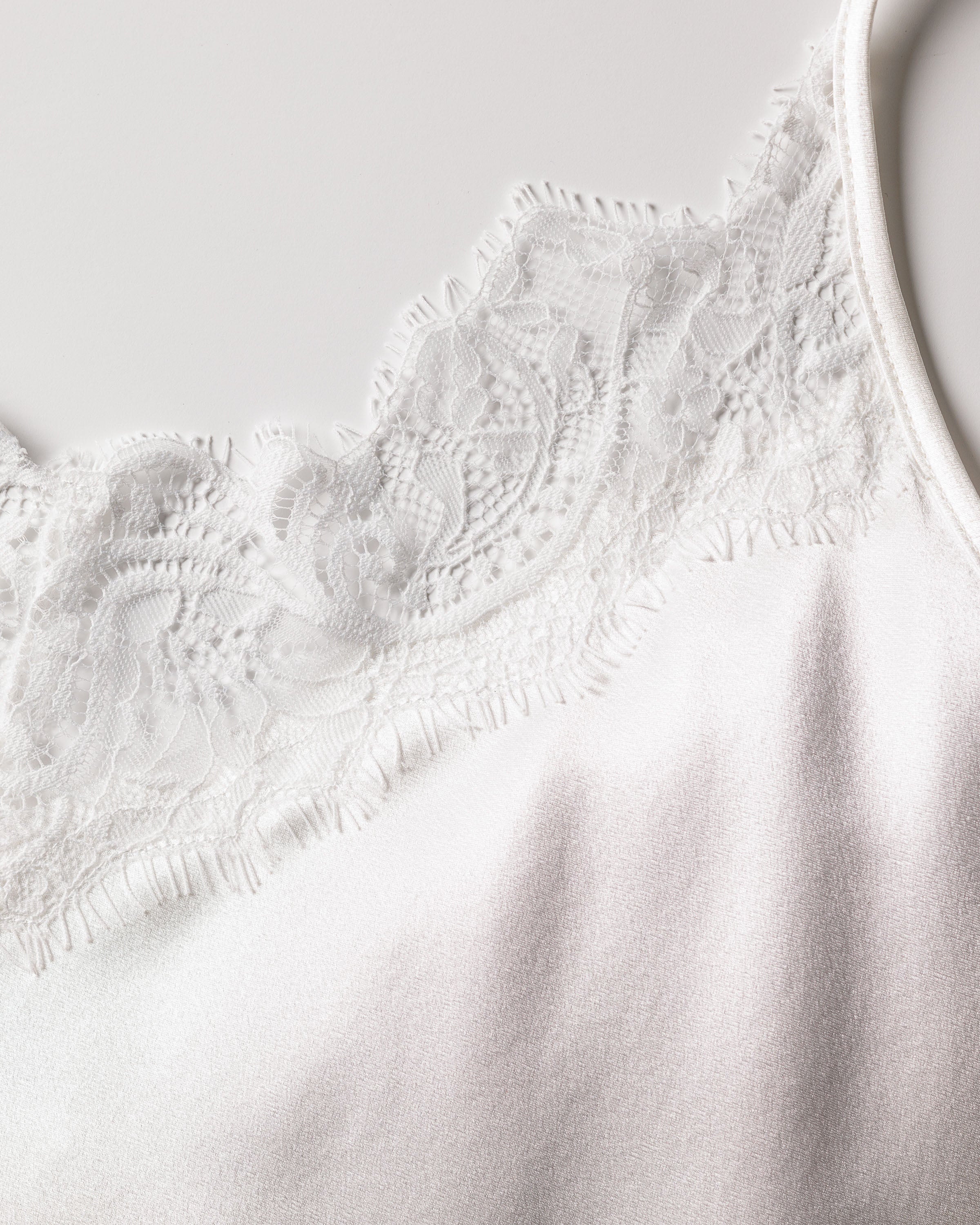 Close-up of Petite Plumes Womens Silk Lace Slip Dress in White, showcasing a delicate lace trim and intricate floral patterns that enhance its minimalist fantasy against the smooth fabric.