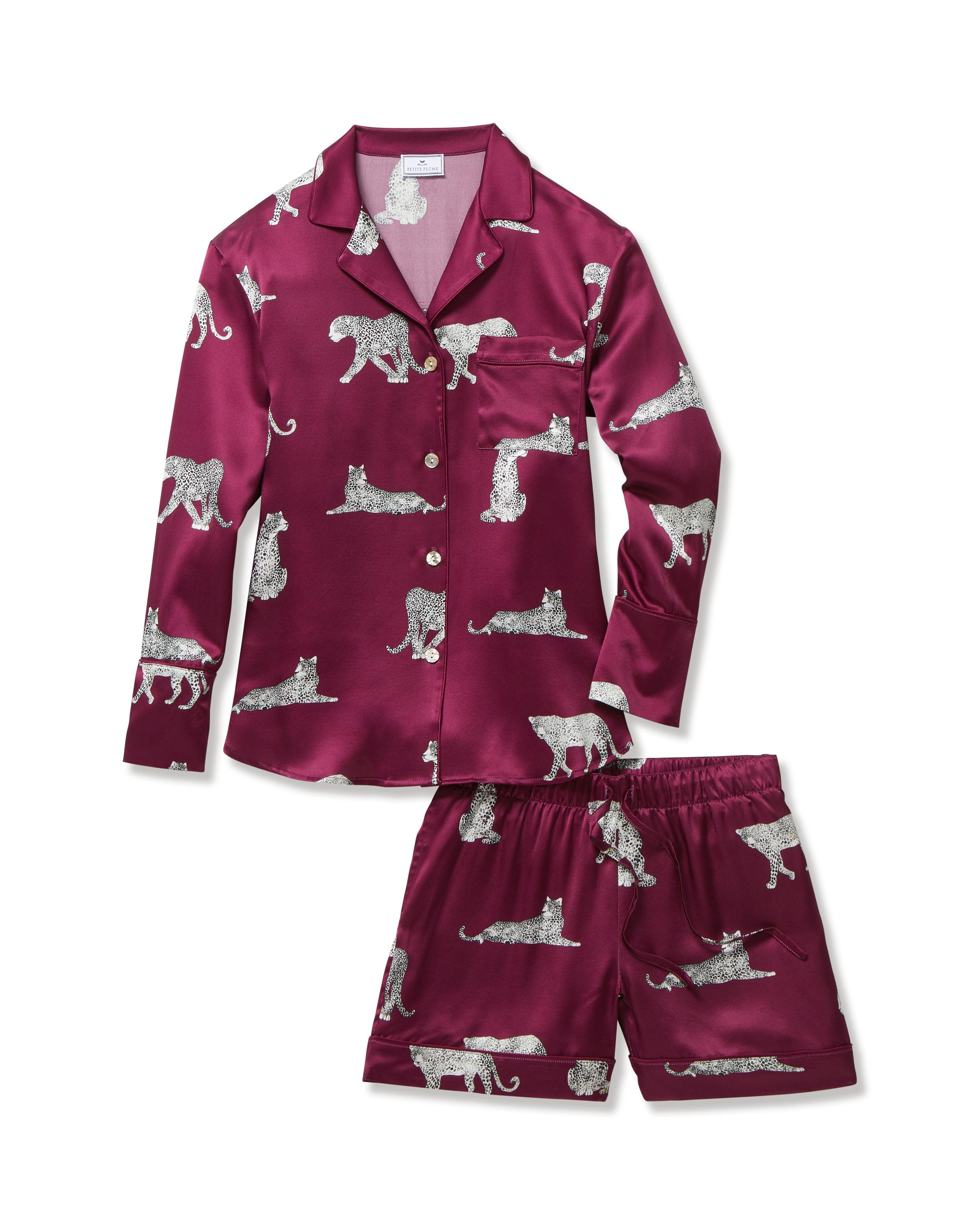 The Women's Silk Long Sleeve Short Set in Merlot Panthère features a dark red satin pajama set with a button-up top and shorts, adorned with white illustrated leopards in various poses.