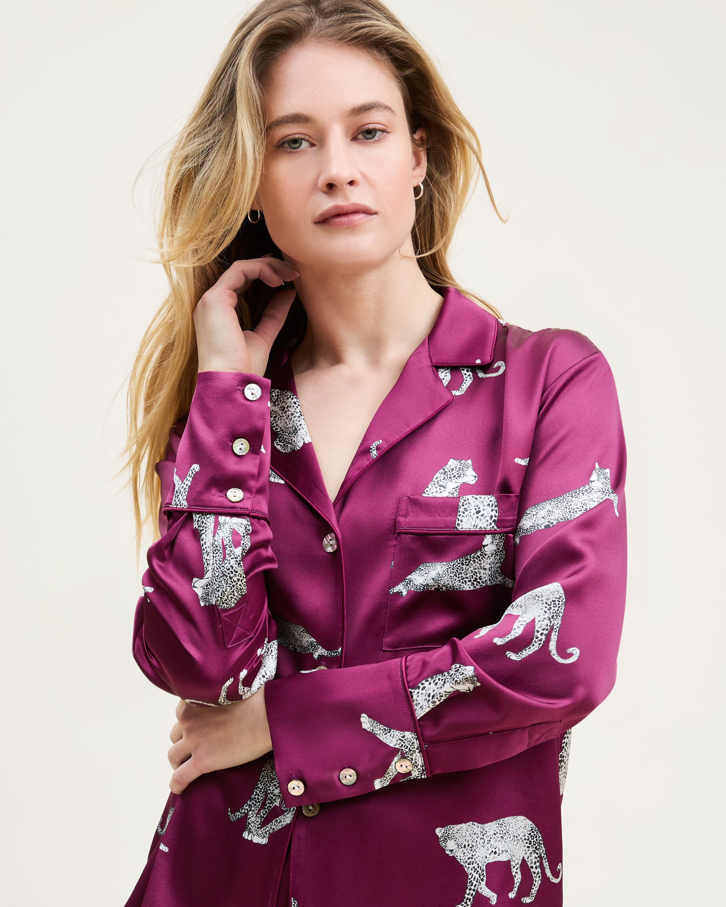 The Women's Silk Long Sleeve Short Set in Merlot Panthère features a dark red satin pajama set with a button-up top and shorts, adorned with white illustrated leopards in various poses.
