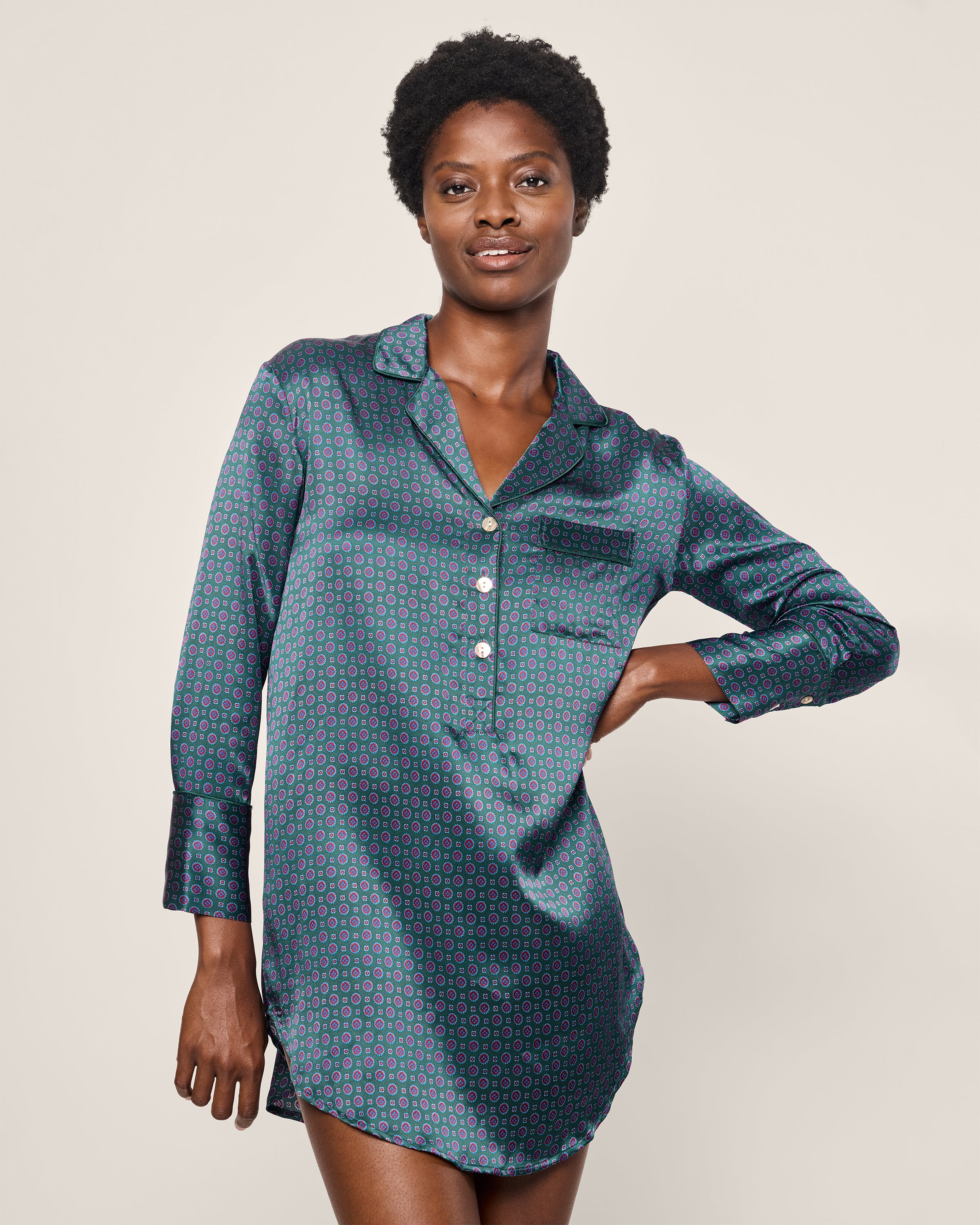 A person poses with a hand on their hip, wearing Petite Plumes Womens Silk Nightshirt in Emerald Foulard and a stylish neck scarf, against a plain, light-colored background that highlights the elegance of Mulberry silk in their outfit.