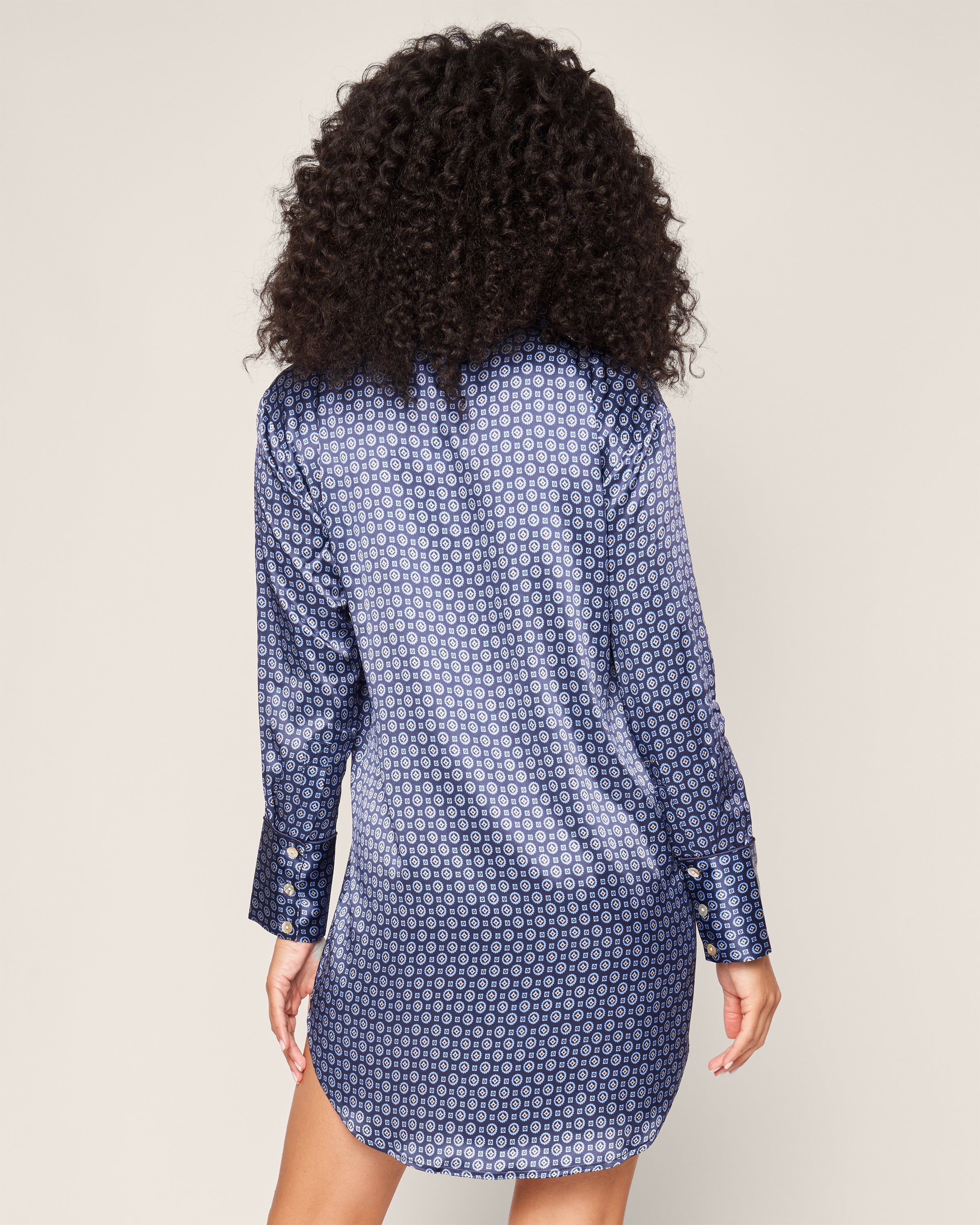 A woman with curly hair, wearing a Petite Plume Womens Silk Nightshirt in Midnight Foulard, is facing away.