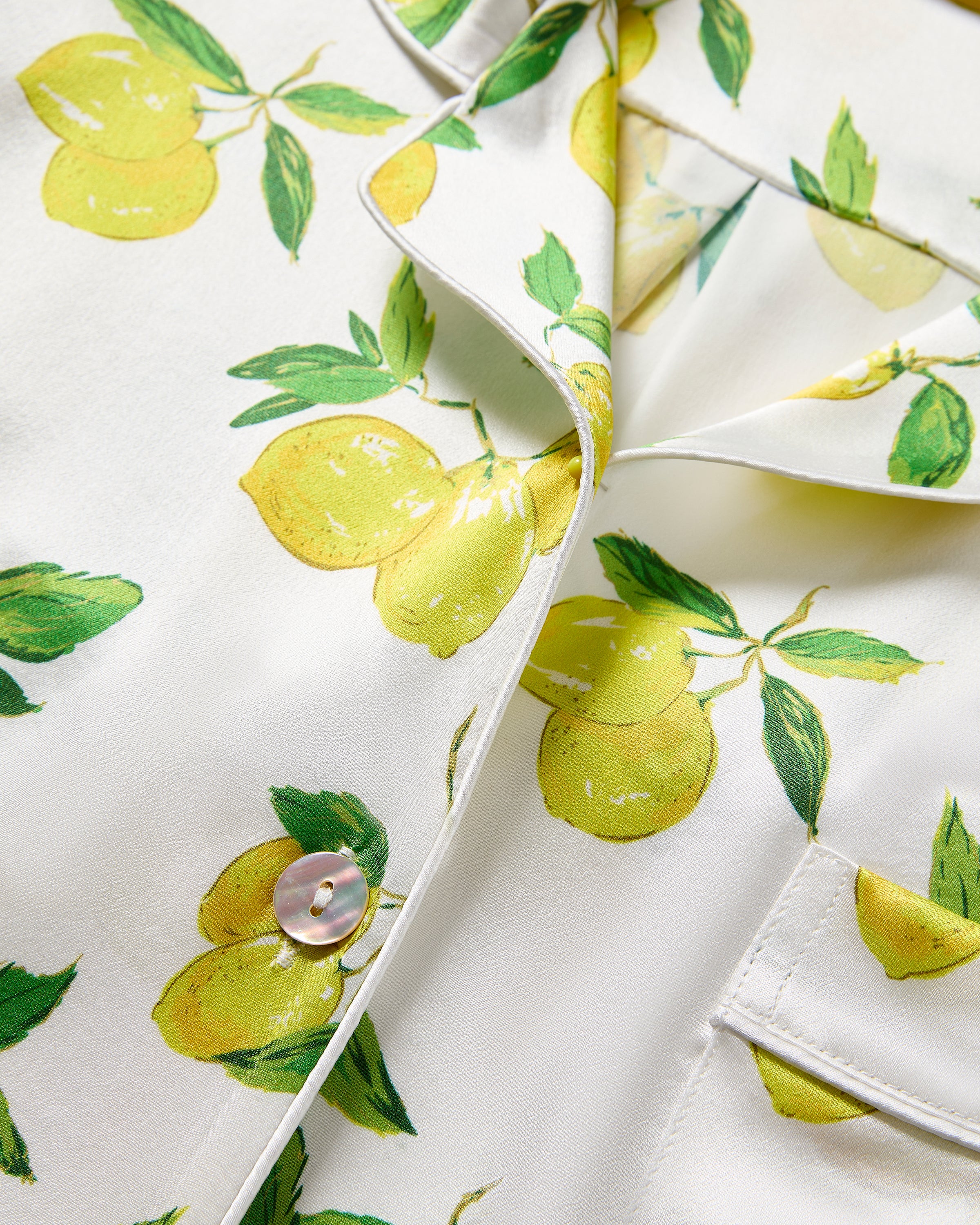 Close-up of a limited-edition Womens Silk Pajama Set in Amalfi Lemons by Petite Plume, featuring lemons with green leaves. The set includes a button-down top with shiny buttons and a breast pocket, blending style and charm.