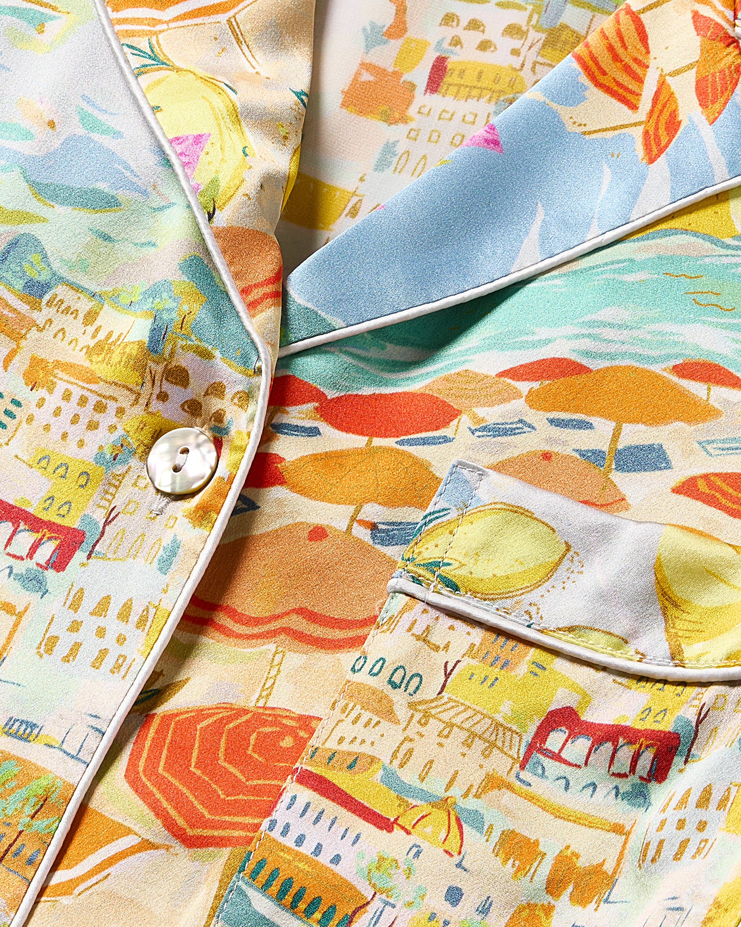 Close-up of Petite Plumes Womens Silk Pajama Set in La Dolce Vita, featuring a colorful abstract pattern in soft blue and orange on mulberry silk with white piping, a pocket, and a button. This luxurious sleepwear exudes elegance.