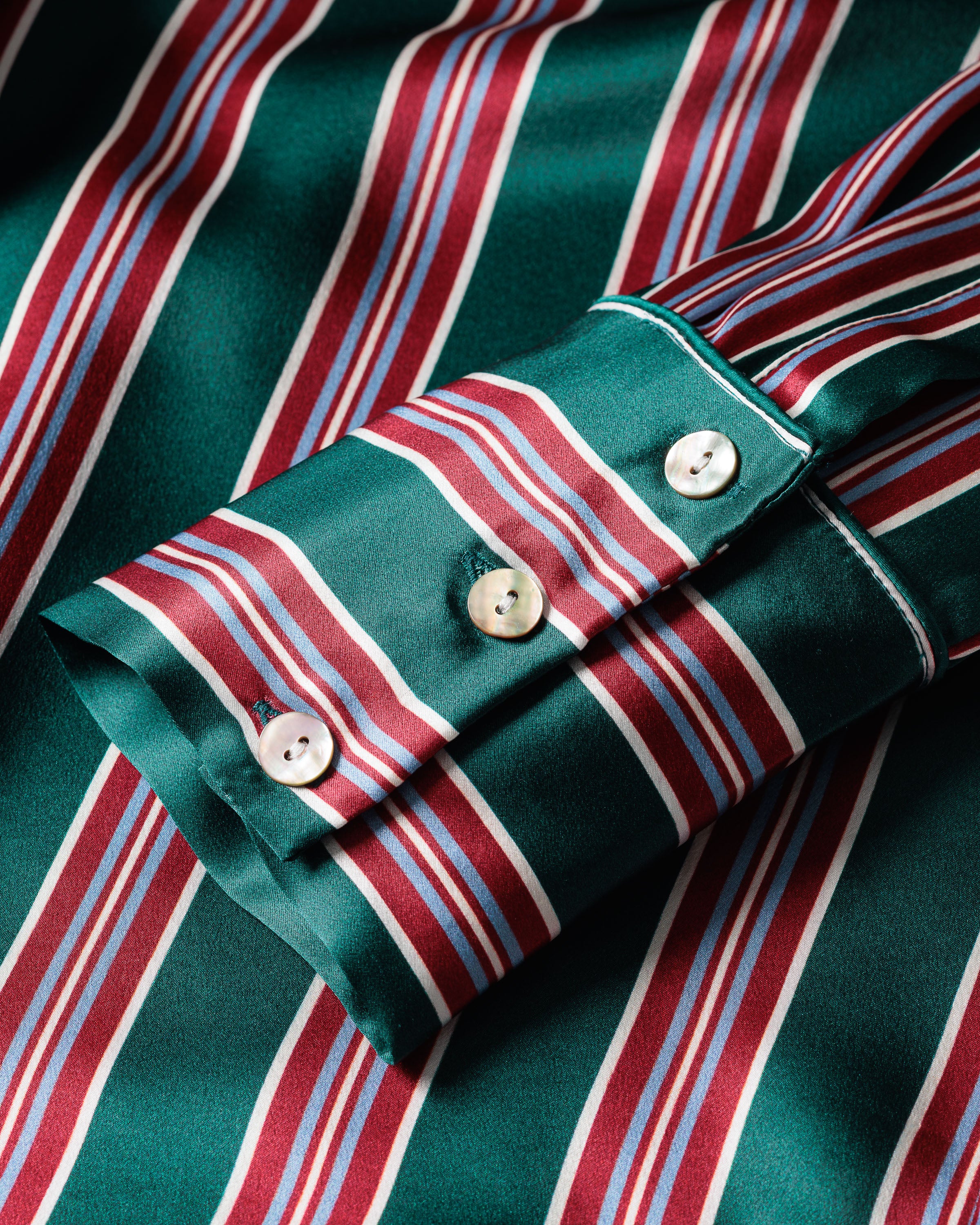 Close-up of the Womens Silk Pajama Set in Lancaster Stripe by Petite Plume: green with red, white, and blue vertical stripes. Made from hypoallergenic mulberry silk for a silky texture, it features cuffs with two white buttons—perfect for luxurious sleepwear elegance.