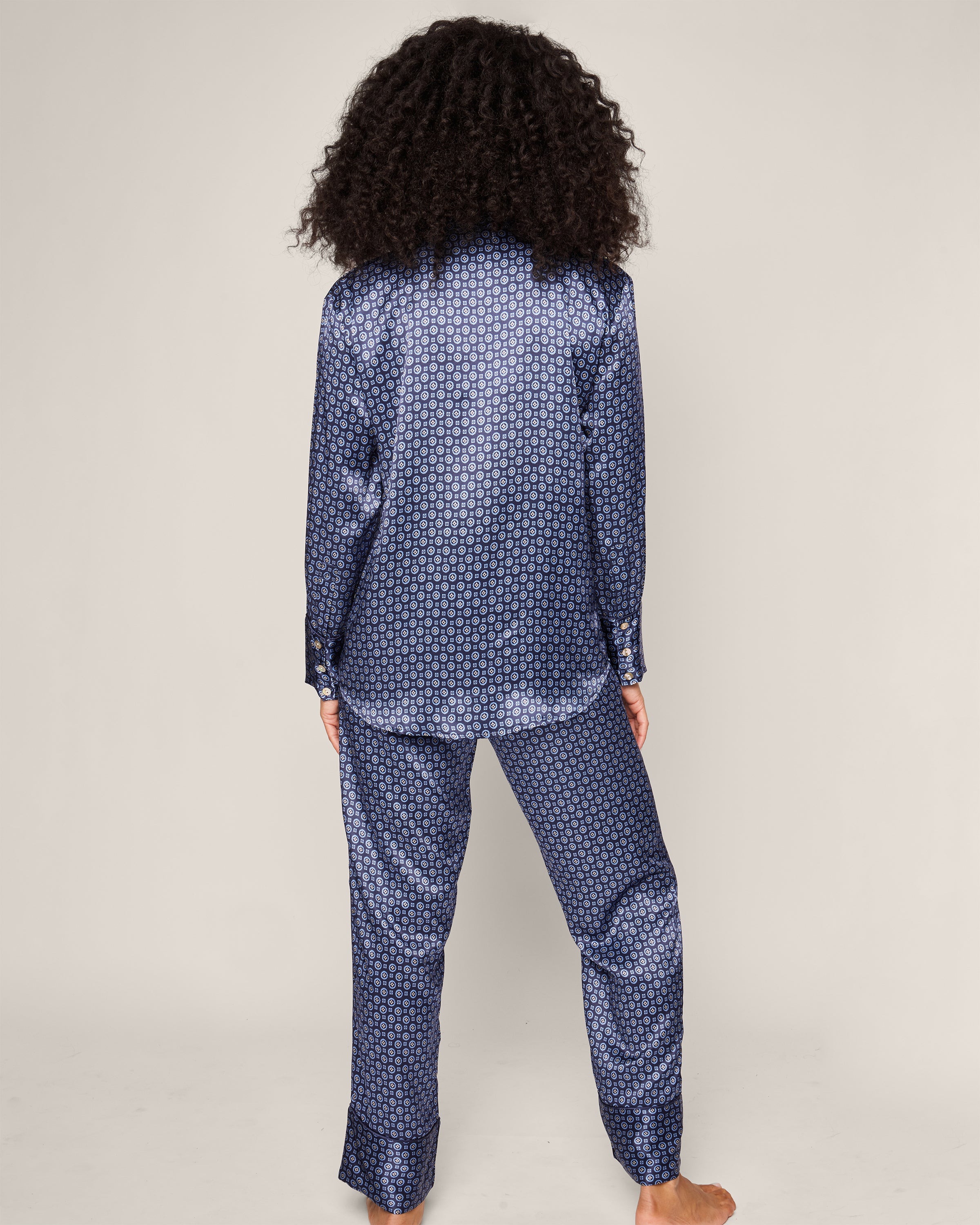 A person with curly hair is wearing the Womens Silk Pajama Set in Midnight Foulard by Petite Plume, crafted from temperature-regulating Mulberry silk. They stand barefoot, back to the camera against a neutral background.