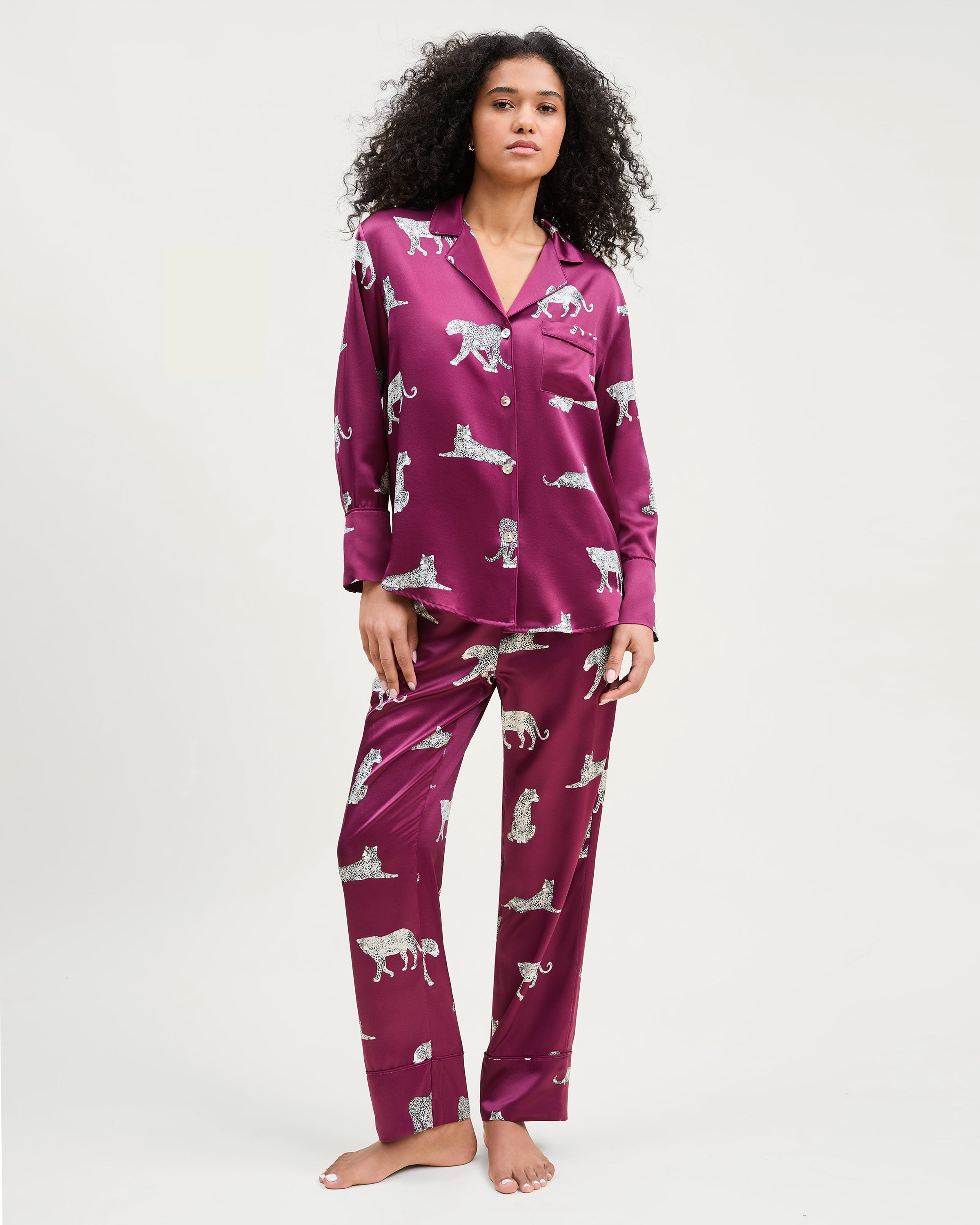 The Women's Silk Pajama Set in Merlot Panthère features a silky, deep magenta button-up shirt and pants adorned with an all-over white illustrated leopard print.
