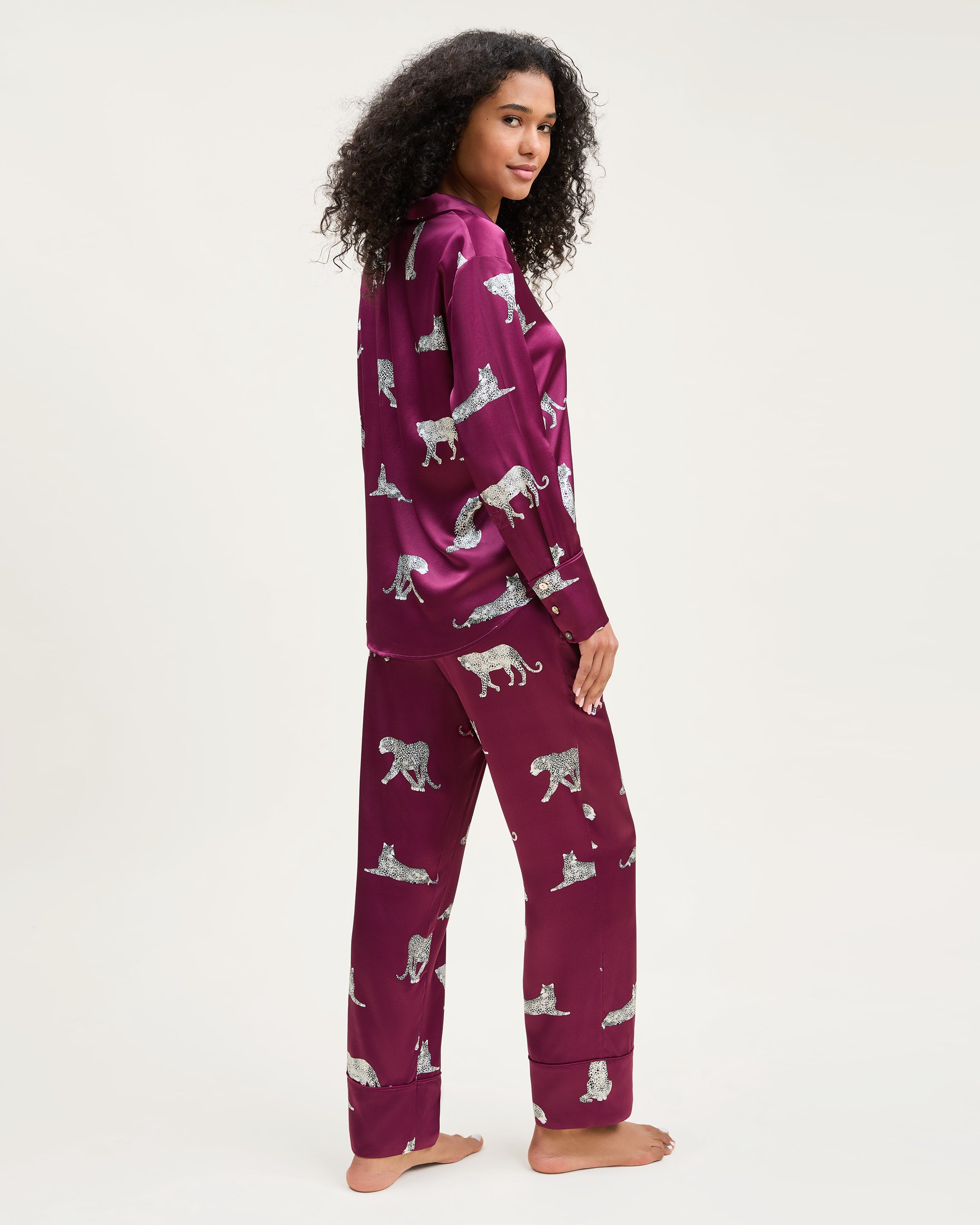 The Women's Silk Pajama Set in Merlot Panthère features a silky, deep magenta button-up shirt and pants adorned with an all-over white illustrated leopard print.