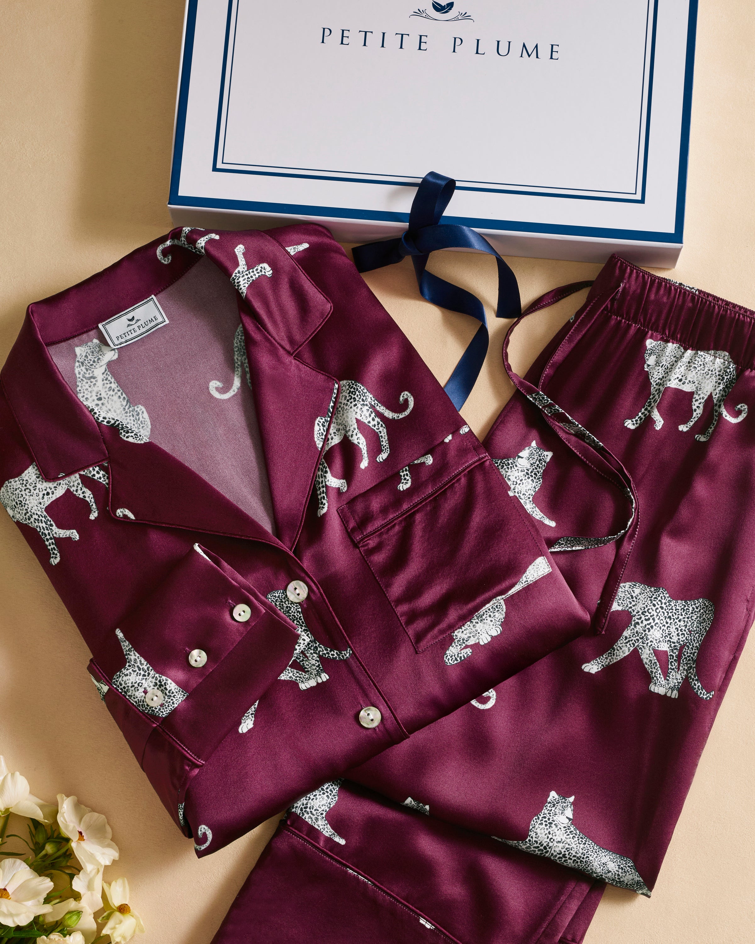 The Women's Silk Pajama Set in Merlot Panthère features a silky, deep magenta button-up shirt and pants adorned with an all-over white illustrated leopard print.