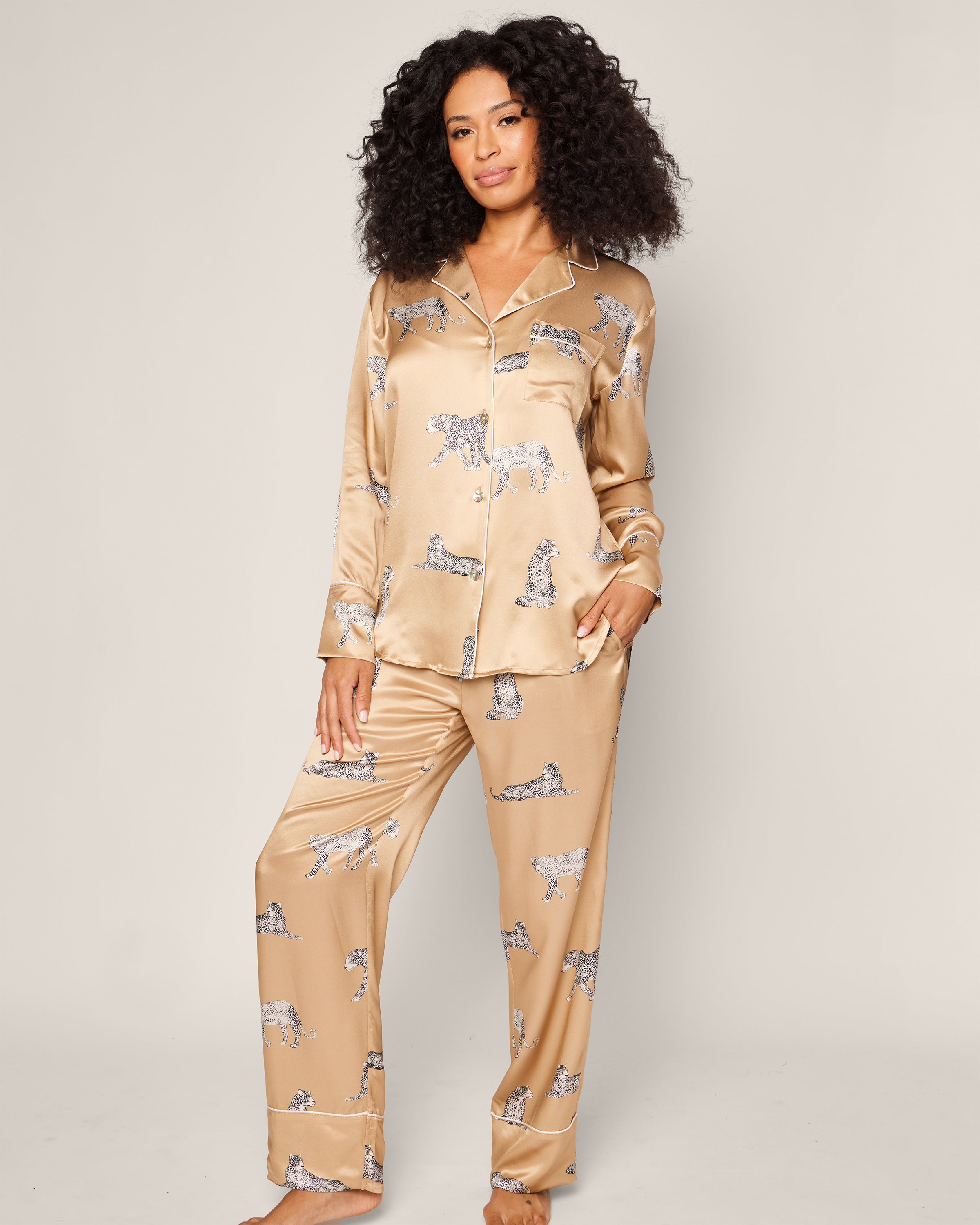 A person with long, curly hair wears the Petite Plume Womens Silk Pajama Set in Panthère Champagne, showcasing its elegant panther motif. The luxurious feel of Mulberry silk stands out against a plain background.