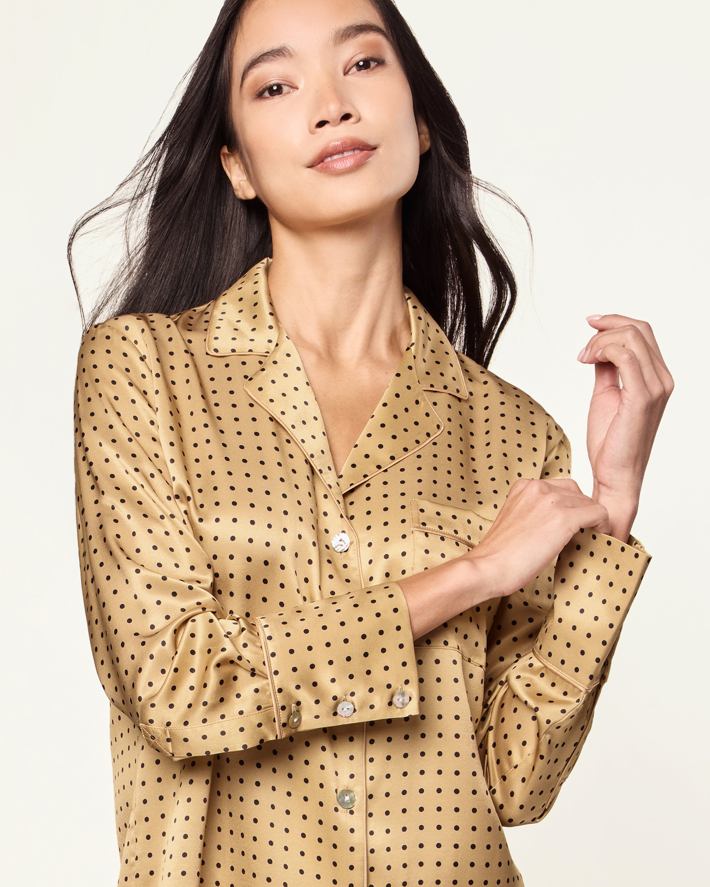 The Women's Silk Pajama Set features a gold fabric with black polka dots, including a long-sleeve button-up top with chest pocket and matching drawstring pants.