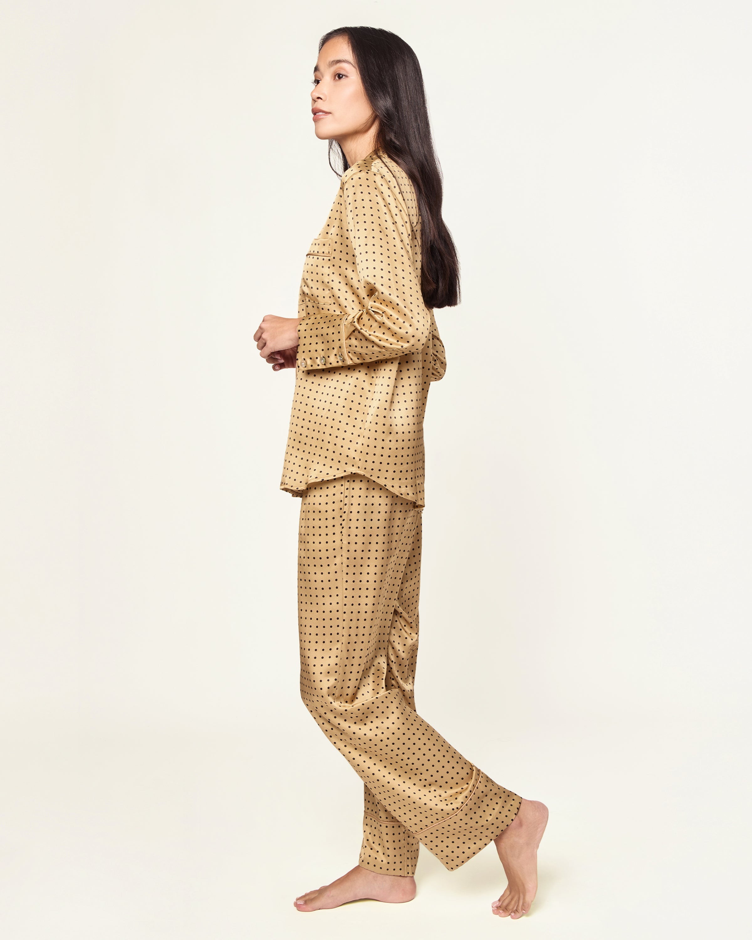 The Women's Silk Pajama Set features a gold fabric with black polka dots, including a long-sleeve button-up top with chest pocket and matching drawstring pants.